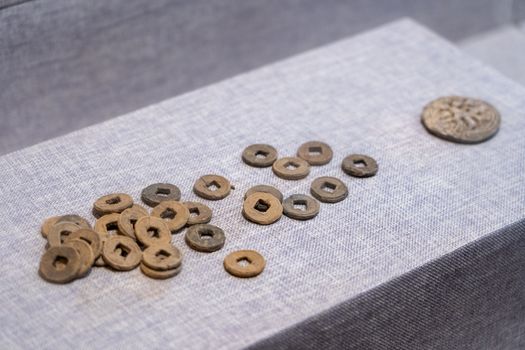 Ancient Chinese coins arranged on a textured fabric platform, showcasing historic currency.