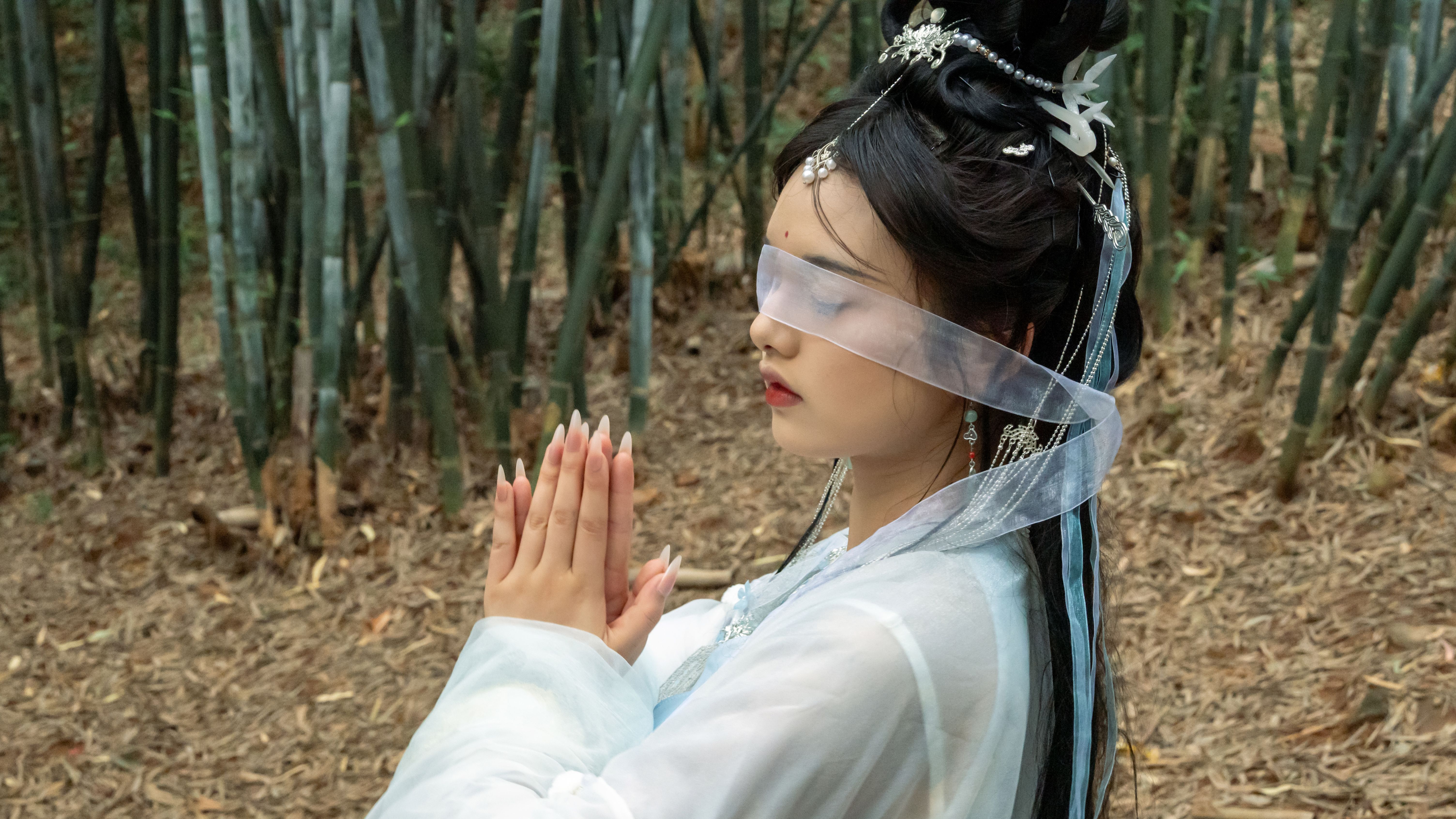 A woman in traditional Asian attire meditates in a serene bamboo forest setting.