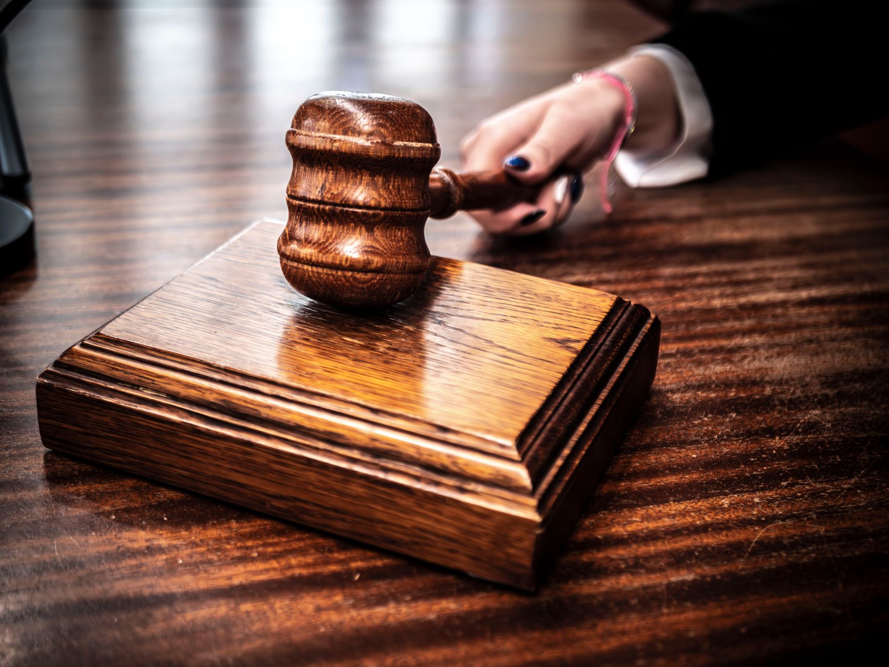 Close-up image of a wooden gavel held by hand on a desk in a courtroom setting.
