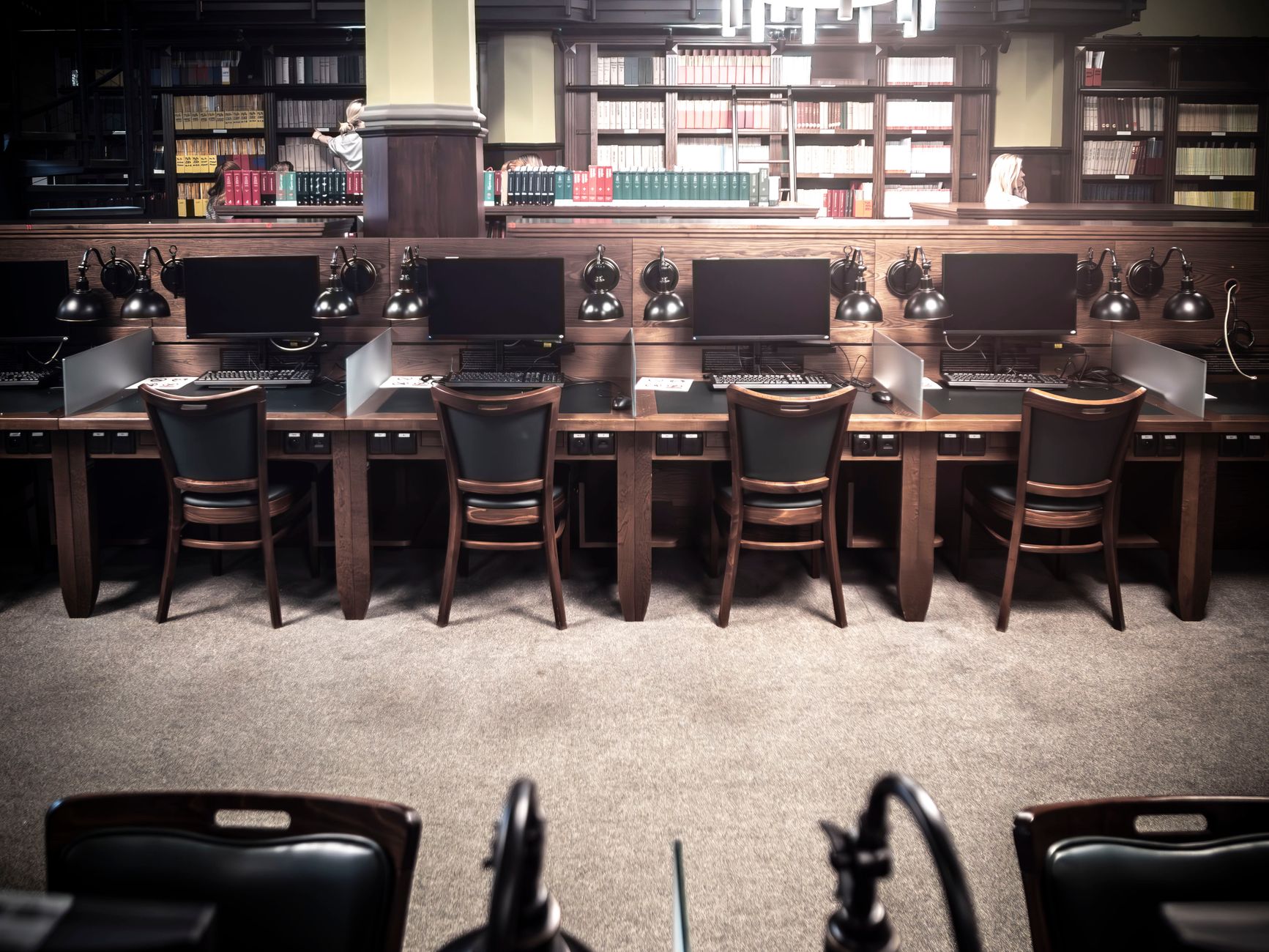 Empty library workstations with computers and vintage lamps, ideal for study or research.