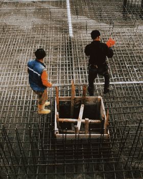 Two workers on a construction site arranging reinforced steel grids.