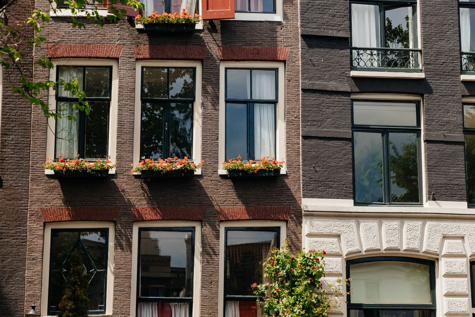 Charming Amsterdam townhouse facade with vibrant flower boxes under sunny skies.