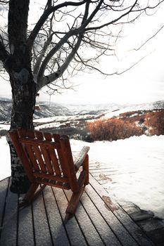 宁静的冬季景观中，一把木制摇椅置于树下，俯瞰着白雪皑皑的山谷
