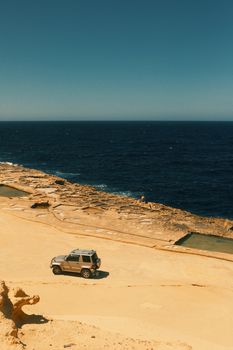 A 4x4 vehicle parked on a sandy coastal terrain near the blue Mediterranean sea under a clear sky.