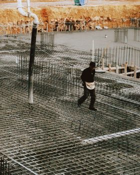 A worker walks on a construction site with reinforced concrete and steel bars, depicting industrial development.