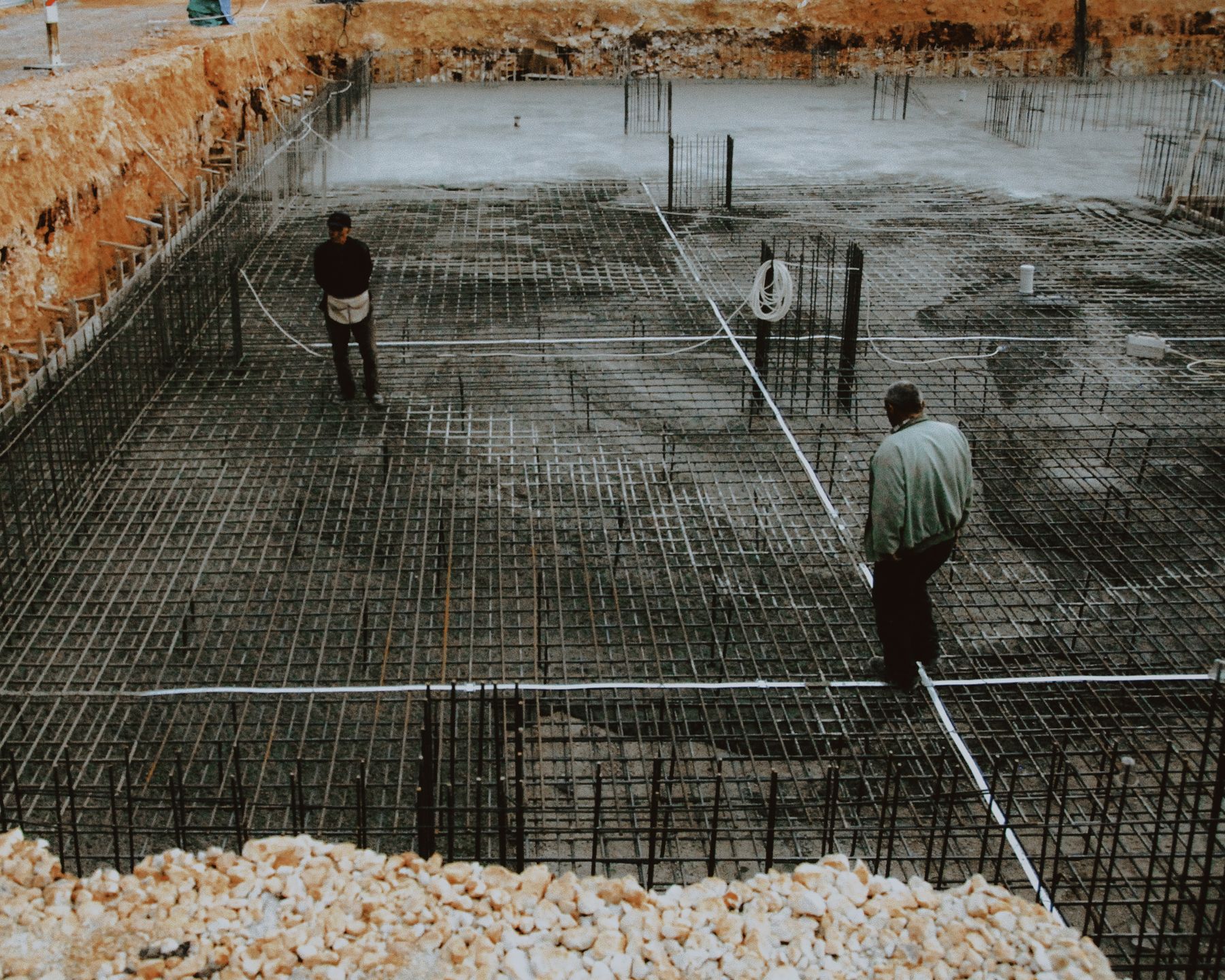 Two workers inspecting a rebar grid before the foundation pour