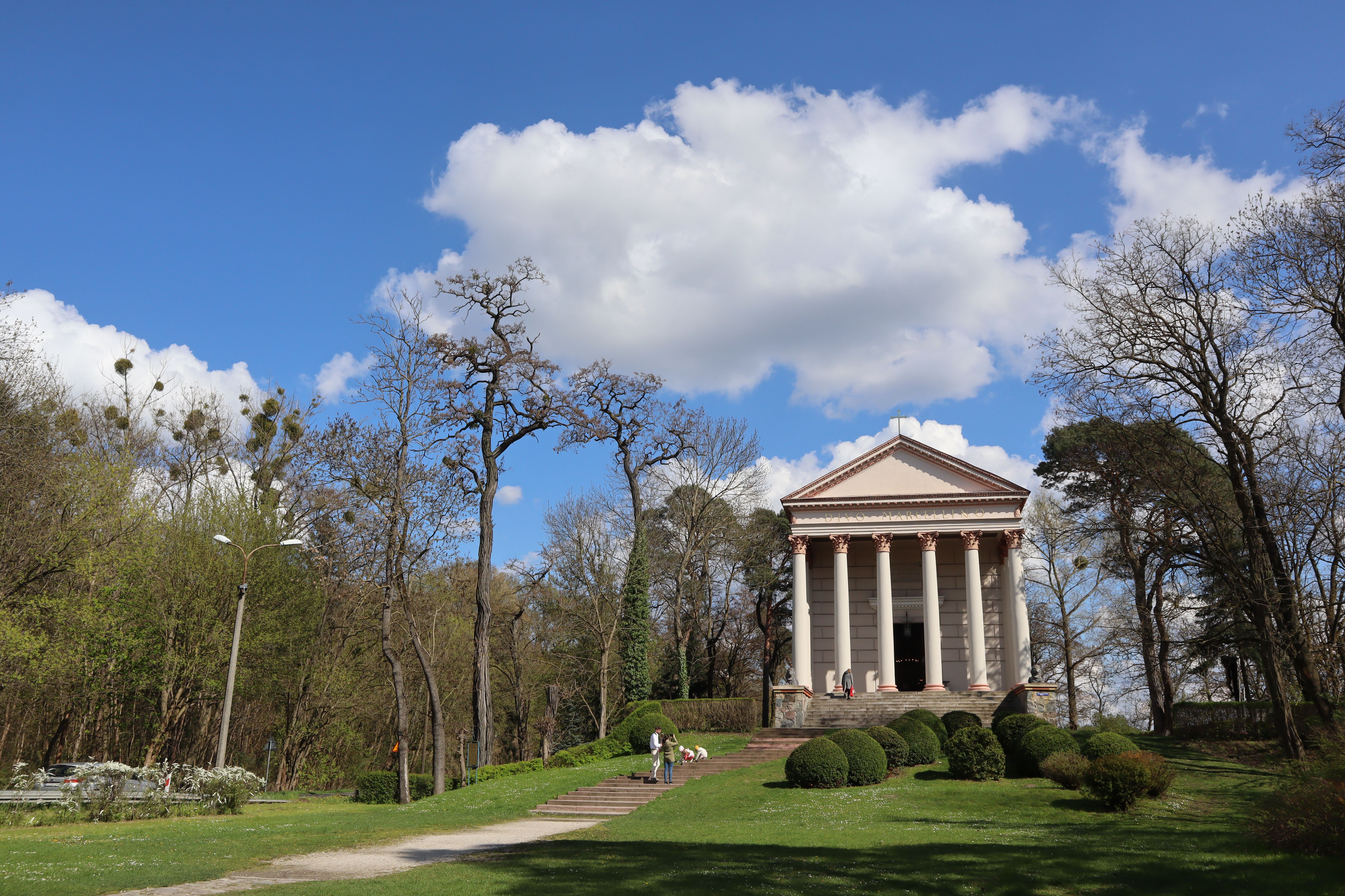 Neoclassical temple surrounded by lush trees under a bright blue sky in a Polish park.