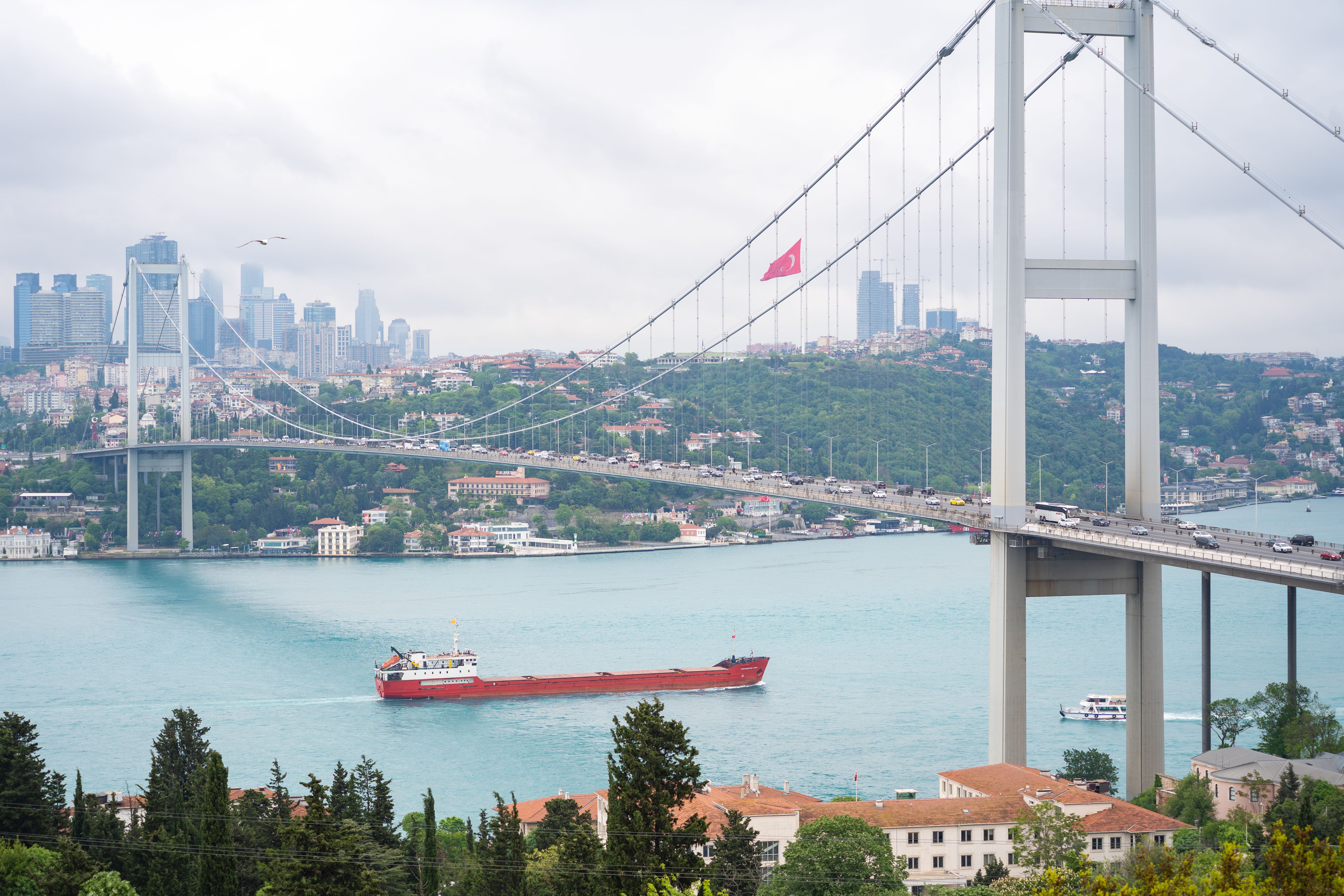 Scenic view of the Bosphorus Bridge with Istanbul skyline and a cargo ship on the turquoise water.