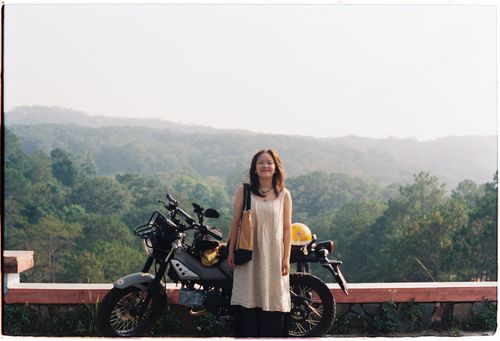 Free A woman stands with a motorcycle against a scenic backdrop in Ho Chi Minh City, Vietnam. Stock Photo