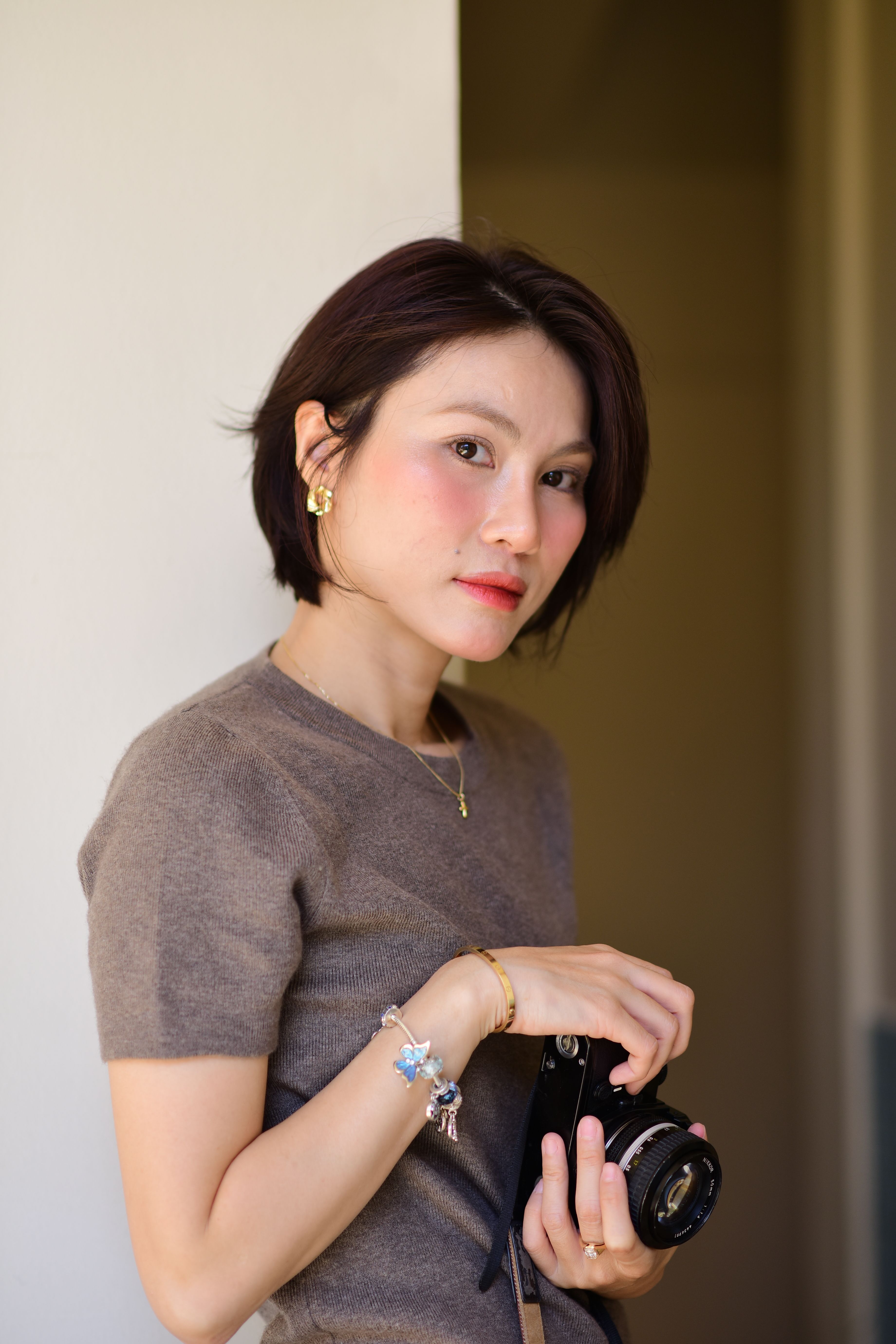 A stylish woman poses with a camera indoors, showcasing minimalistic fashion.