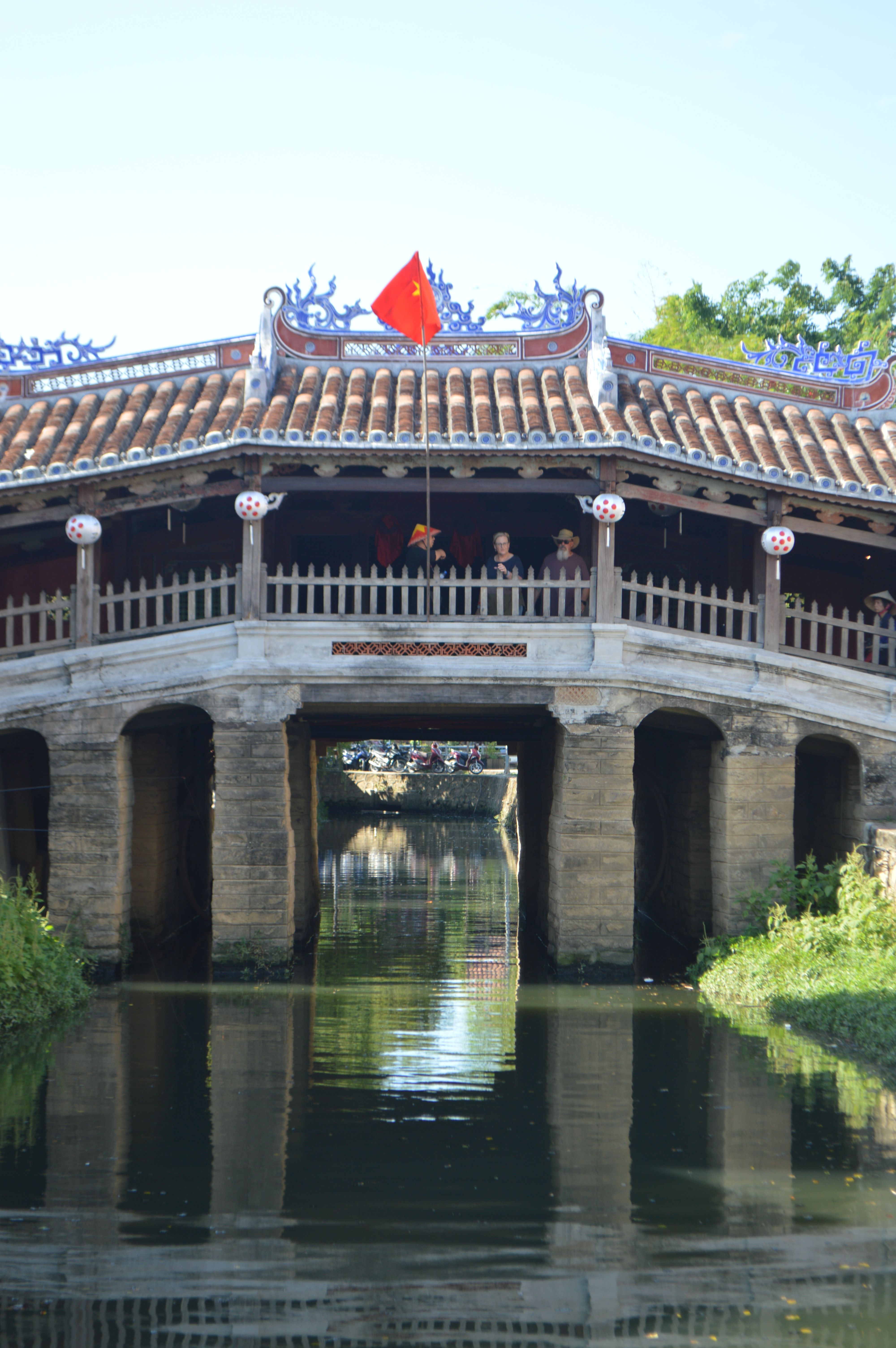 A scenic view of the Japanese Covered Bridge in Hoi An, Vietnam with flags and reflections.