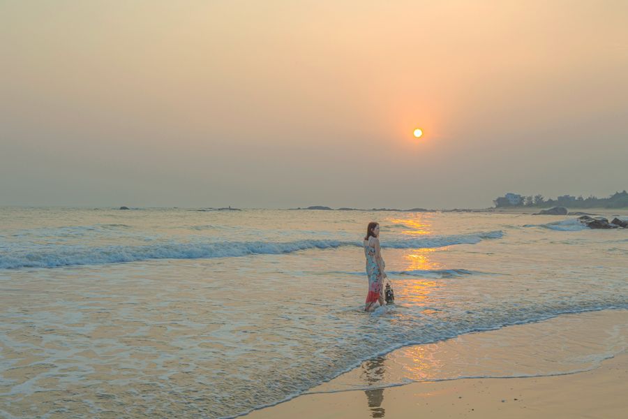 A woman enjoys a peaceful walk along Guangdong's beach at sunset, China.