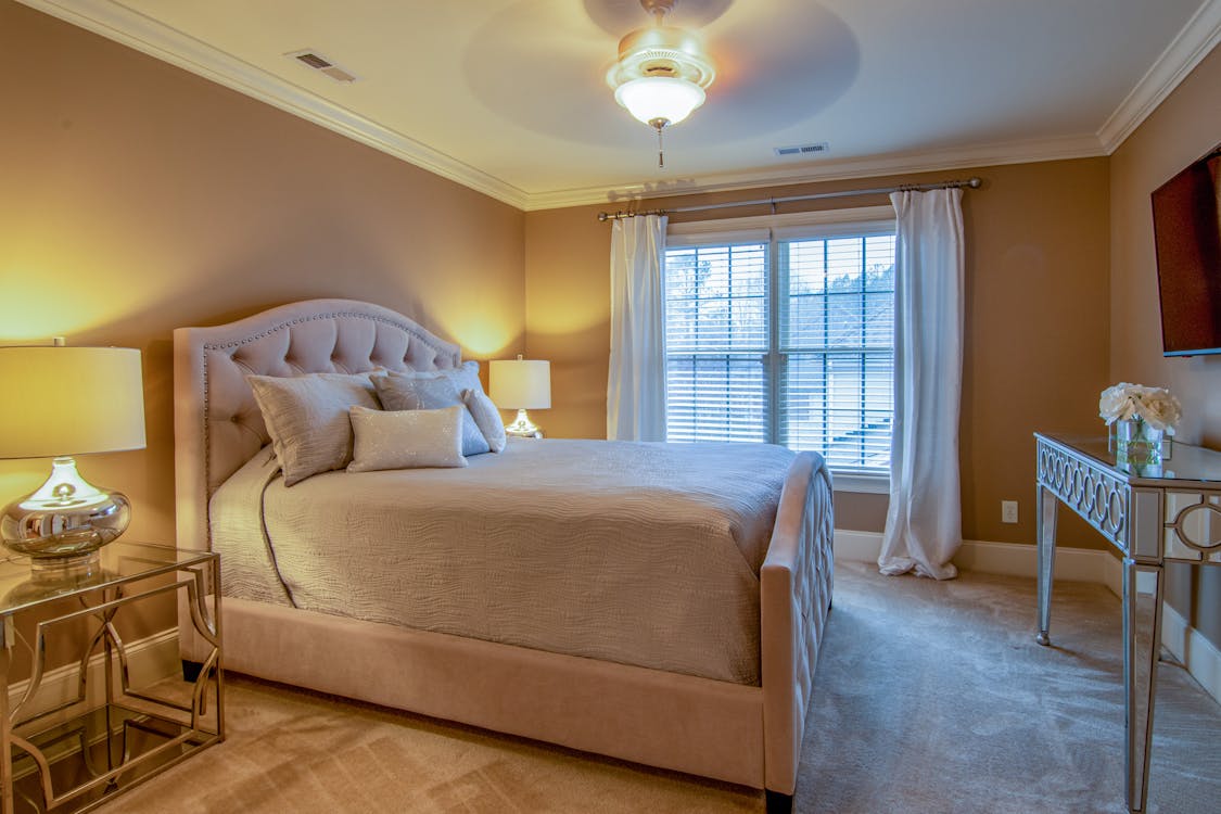 big bed with pillows near the window with shades and curtains