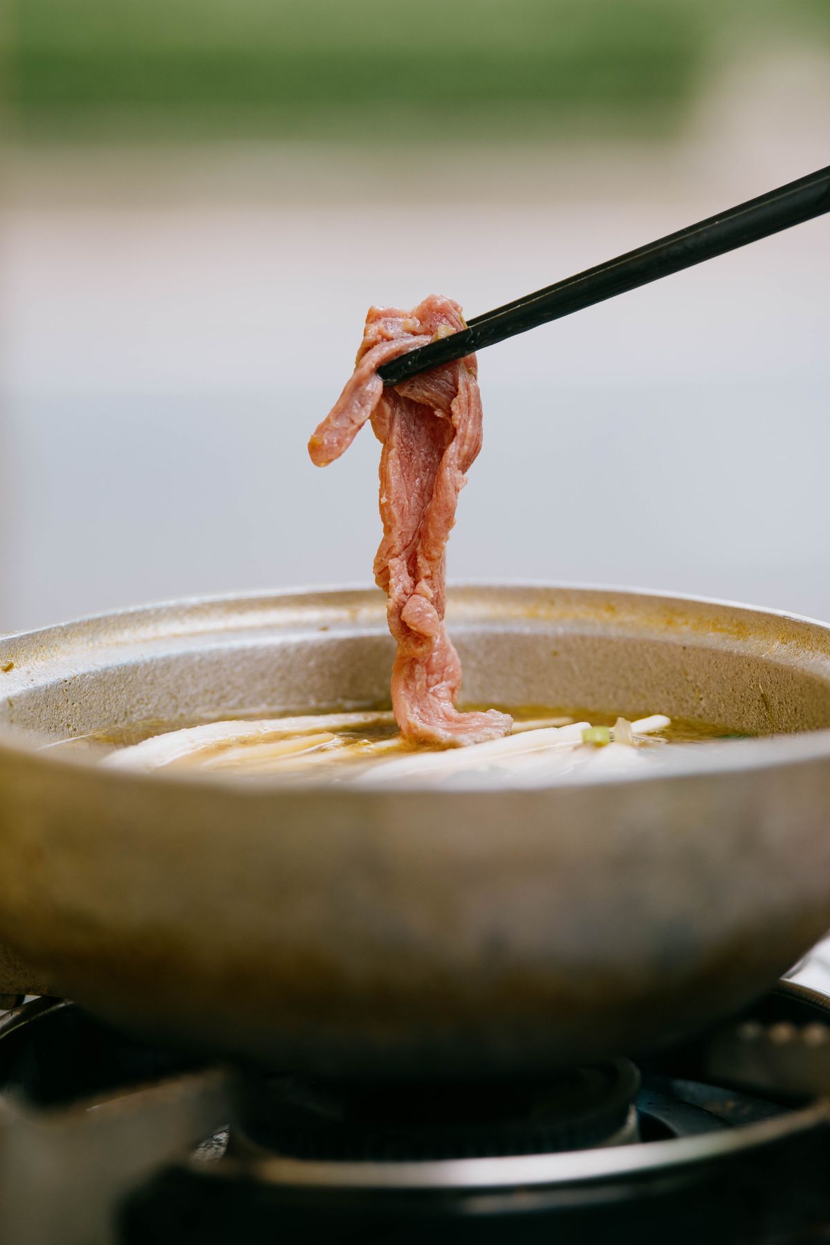 Chopsticks lifting a thin slice of beef from a shabu shabu hot pot