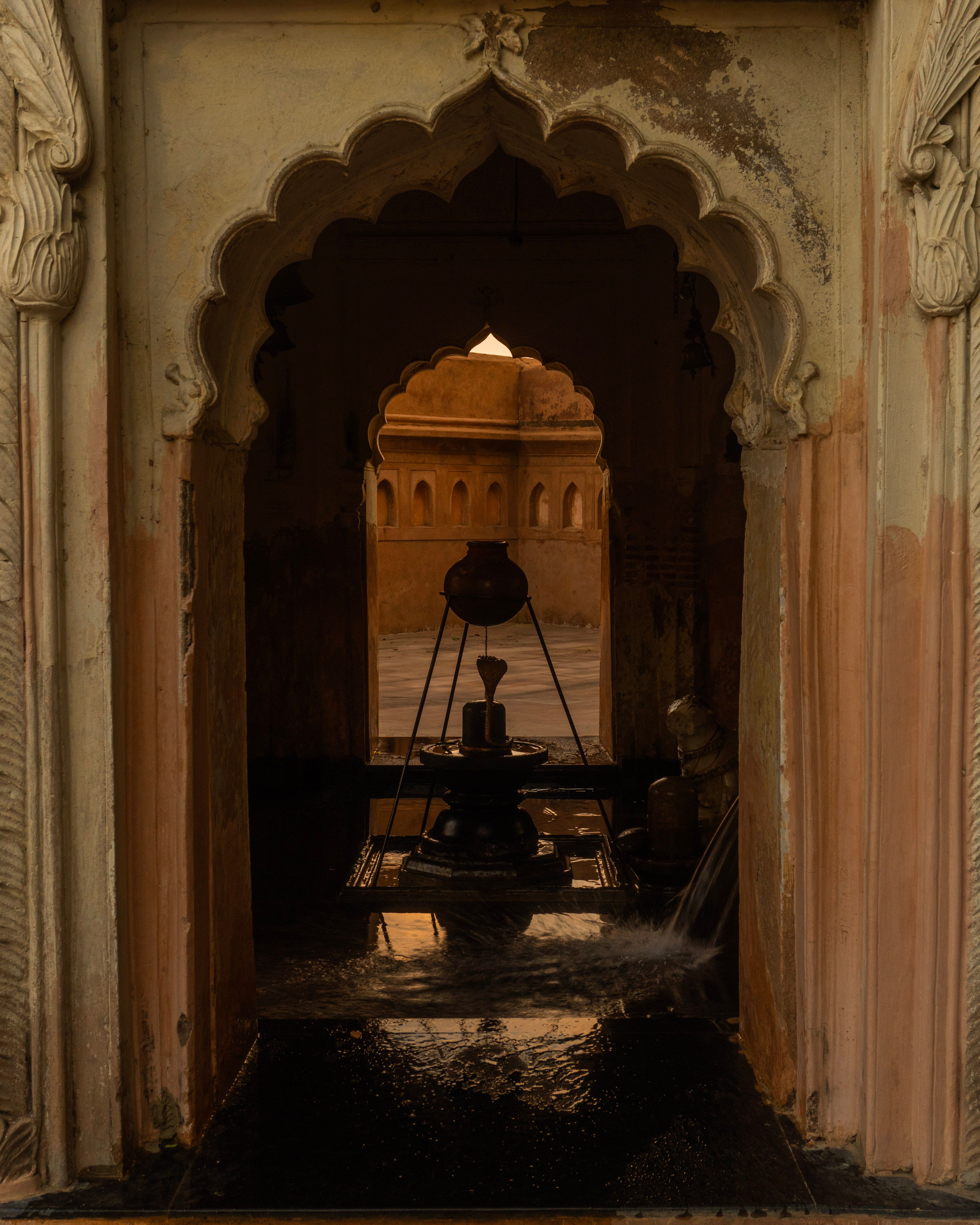 A serene view through an ornate archway leading to an inner temple sanctum with a water feature.