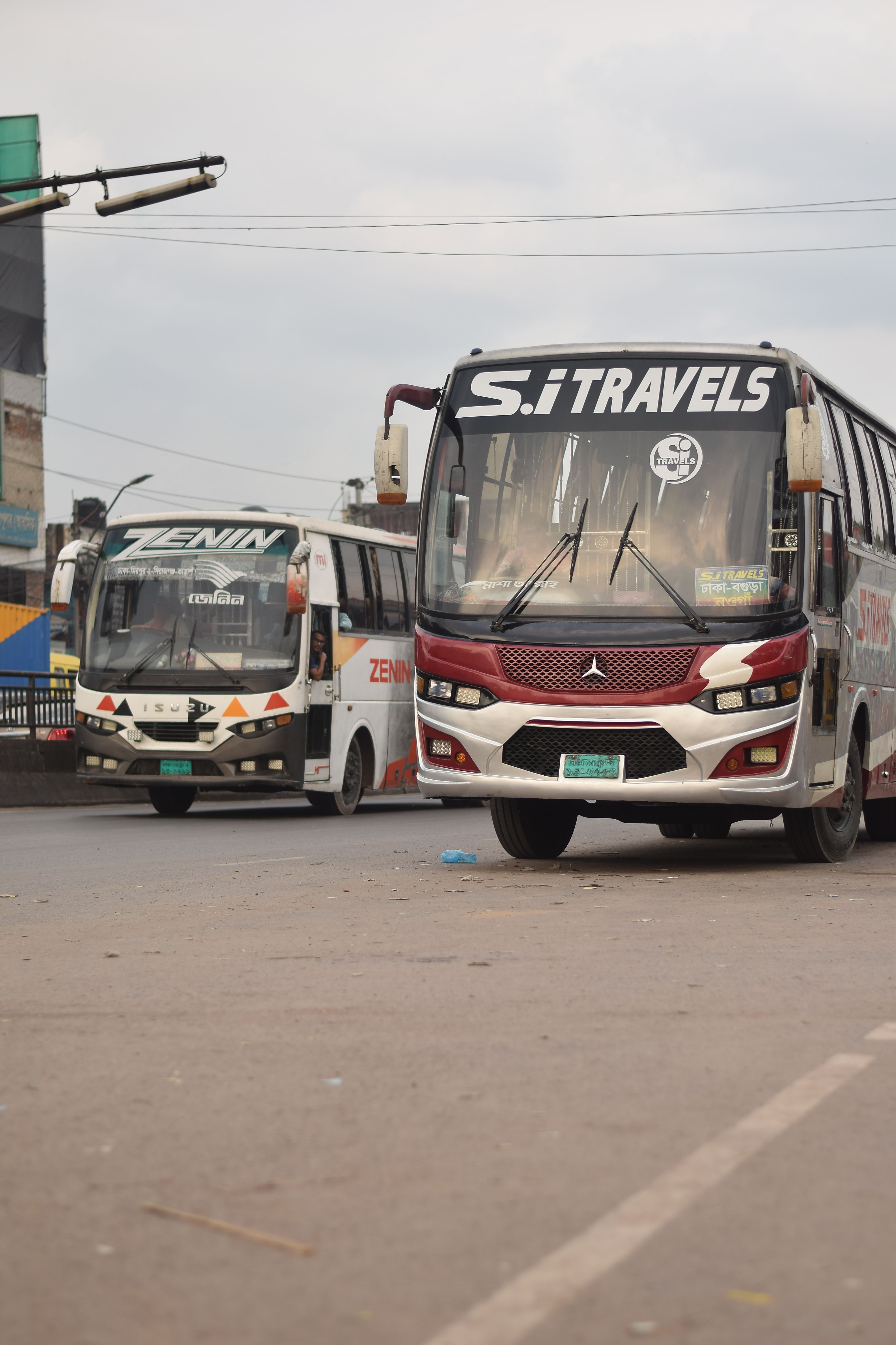 Two public buses driving on a city street in Dhaka, Bangladesh.