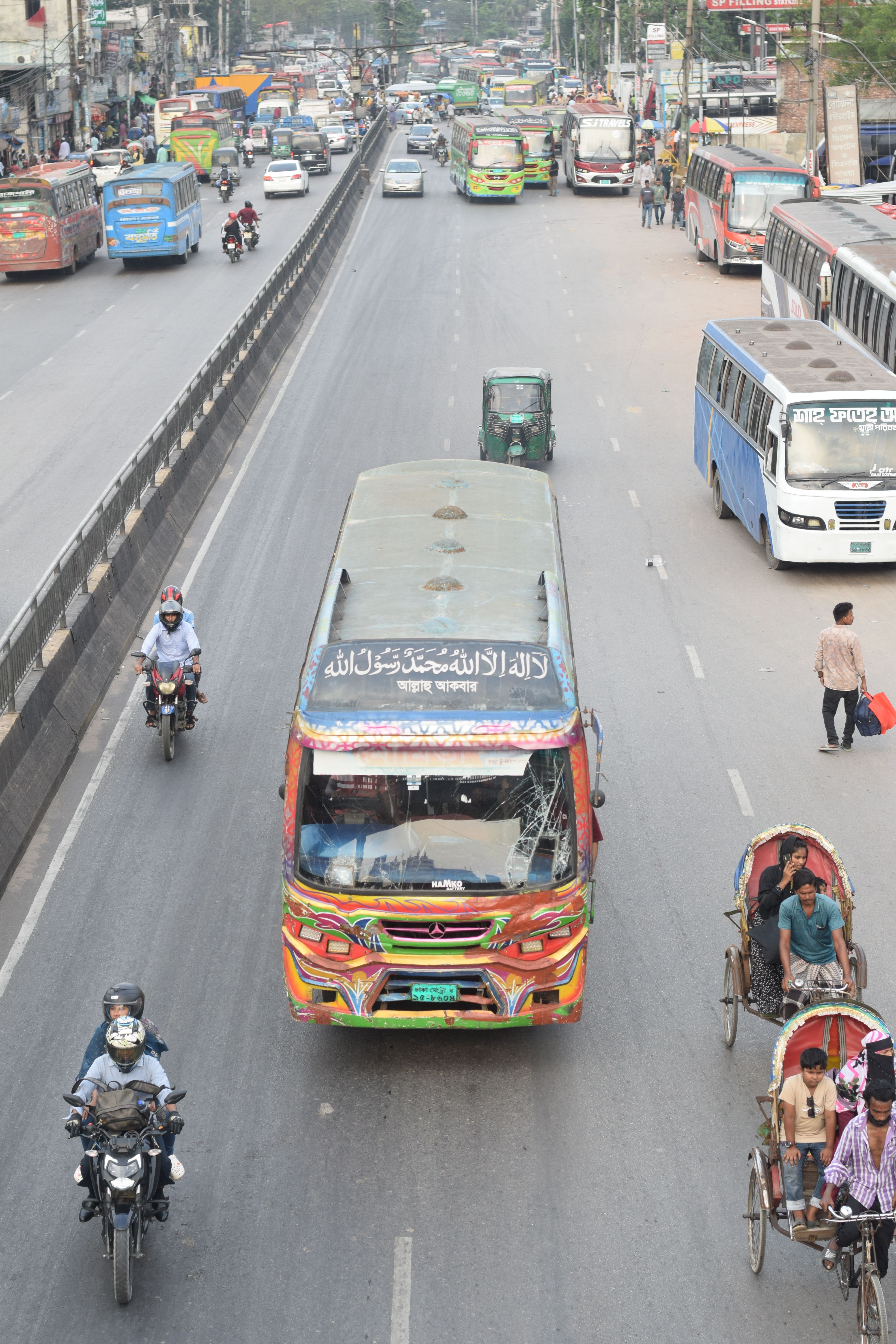 Vibrant traffic scene in Dhaka with buses, motorcycles, and rickshaws on a busy road.