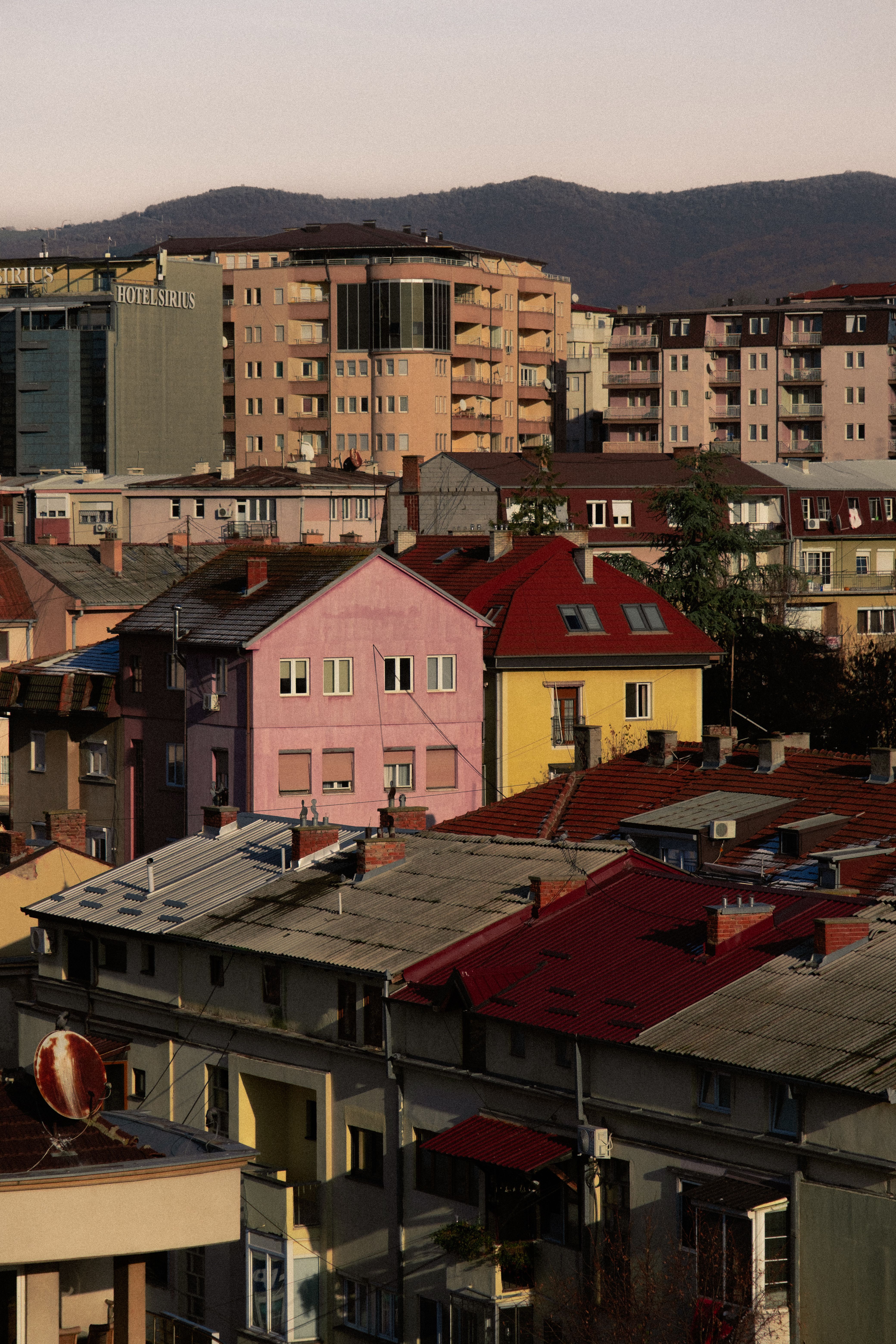 Colorful rooftops and residential buildings in Pristina, Kosova, with mountains in the background.