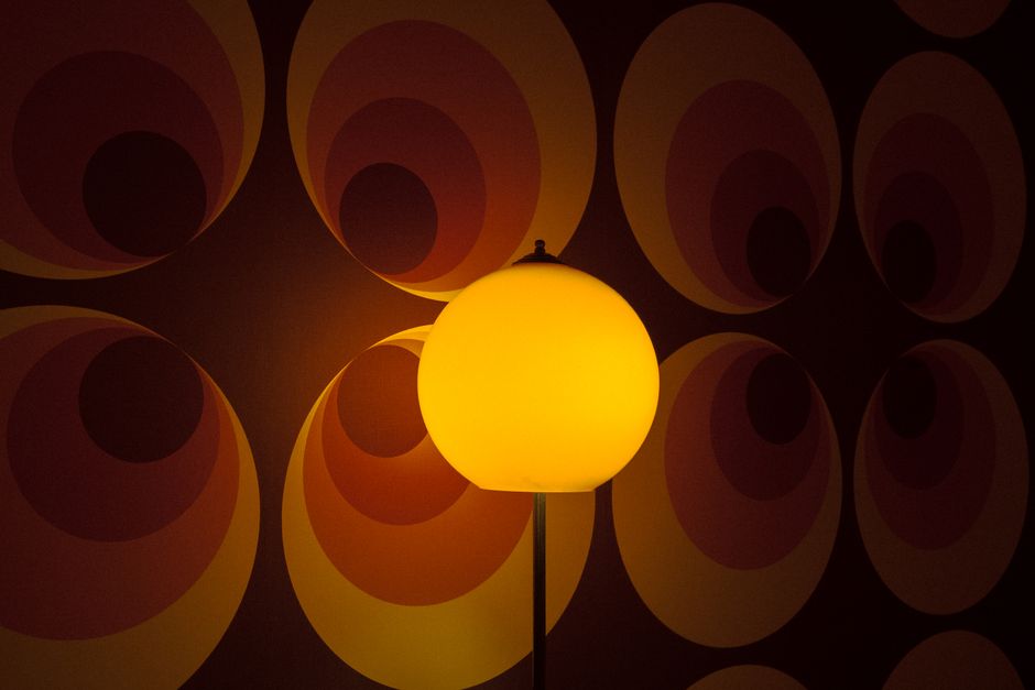 A glowing retro lamp illuminating vintage patterned wallpaper with circular designs in warm tones.