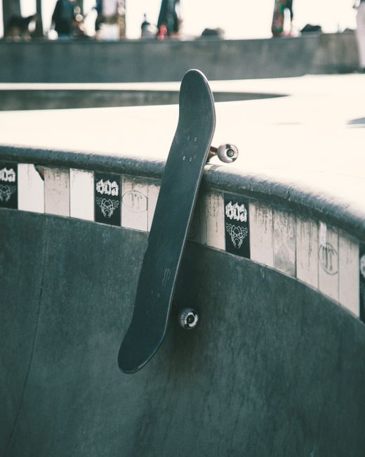 Close-up of a skateboard leaning against a skatepark ramp under daylight.