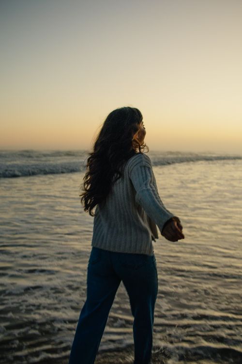 Free A woman walks along the shoreline, enjoying a serene sunset at the beach. Stock Photo