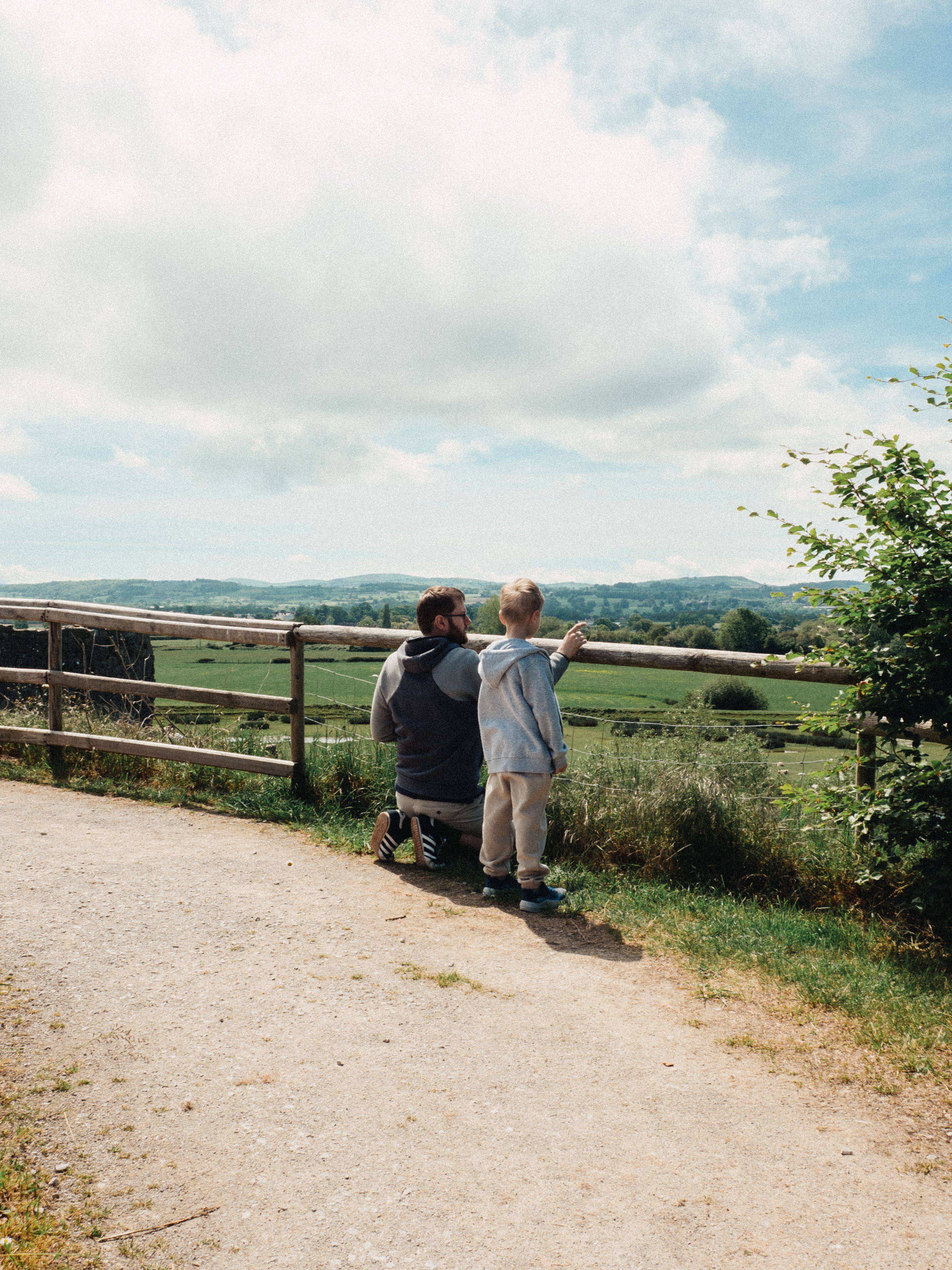A father and son bonding while overlooking a vast rural landscape on a sunny day.