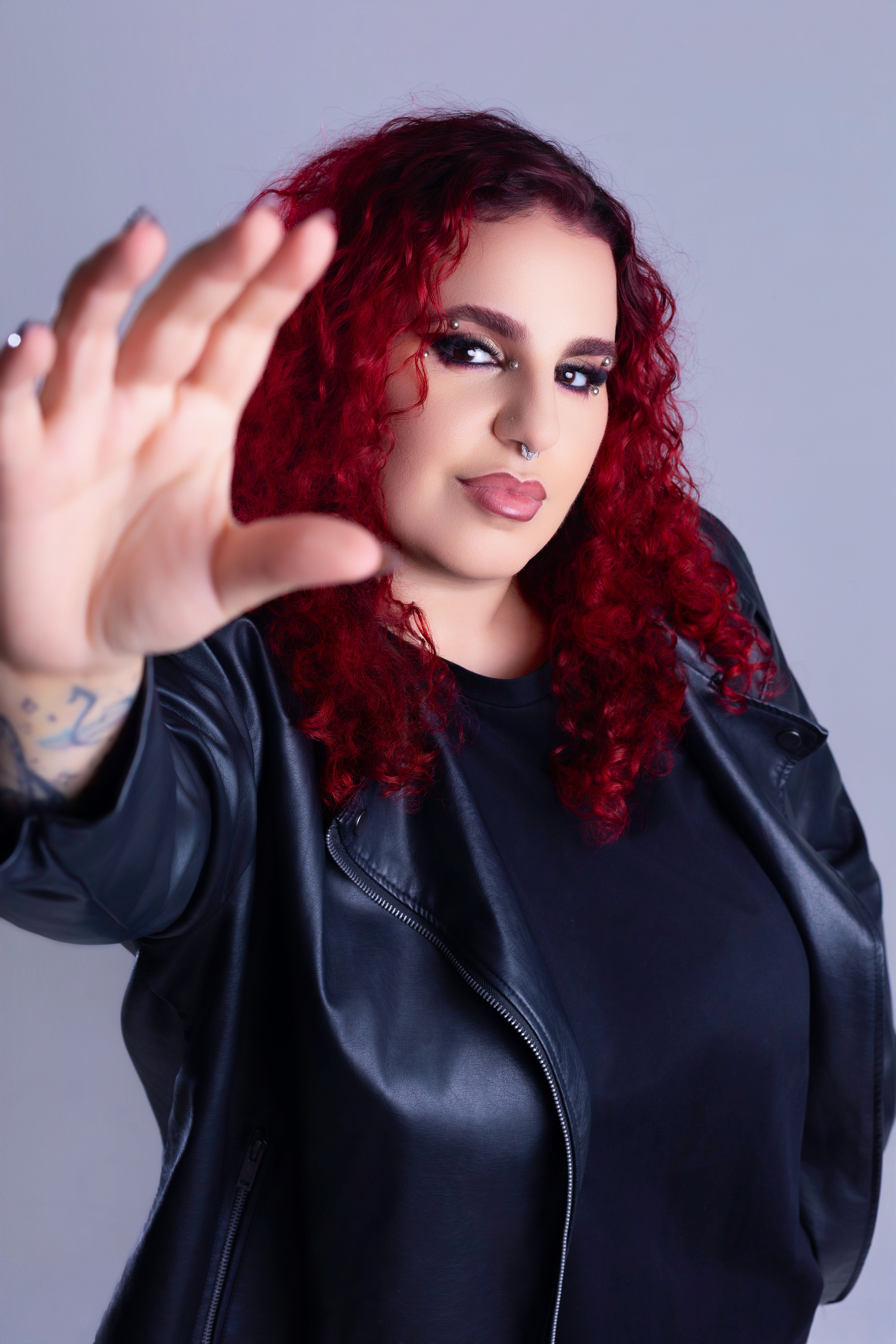 Portrait of a confident woman with red curly hair and a leather jacket against a neutral background.