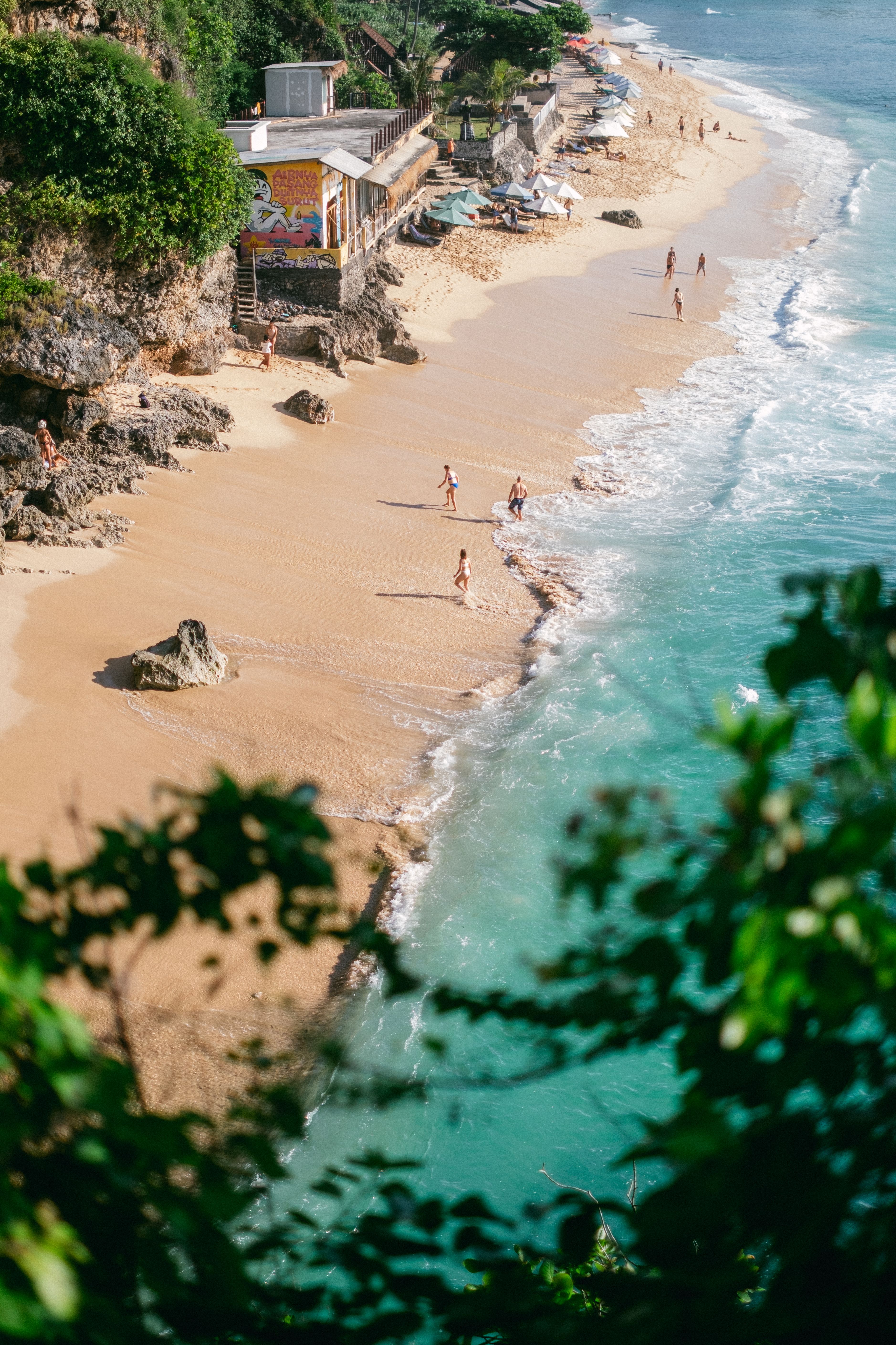 Aerial view of a beautiful tropical beach with clear turquoise waters and people enjoying a sunny day.