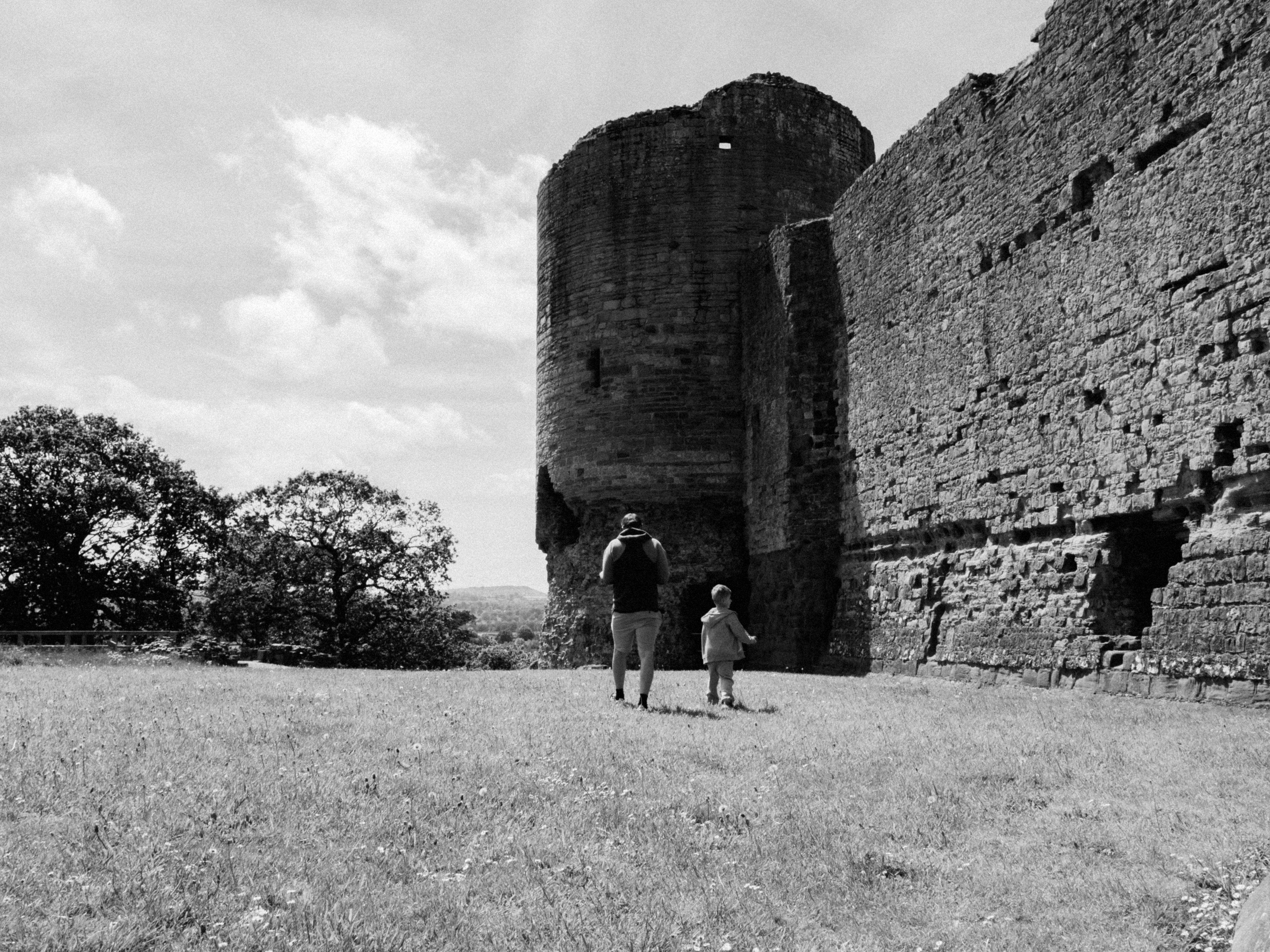 A black and white image of a father and child walking by Rhuddlan Castle in Wales.