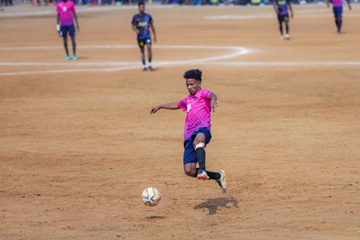 A dynamic scene featuring a young soccer player in action during a match on a dirt field.