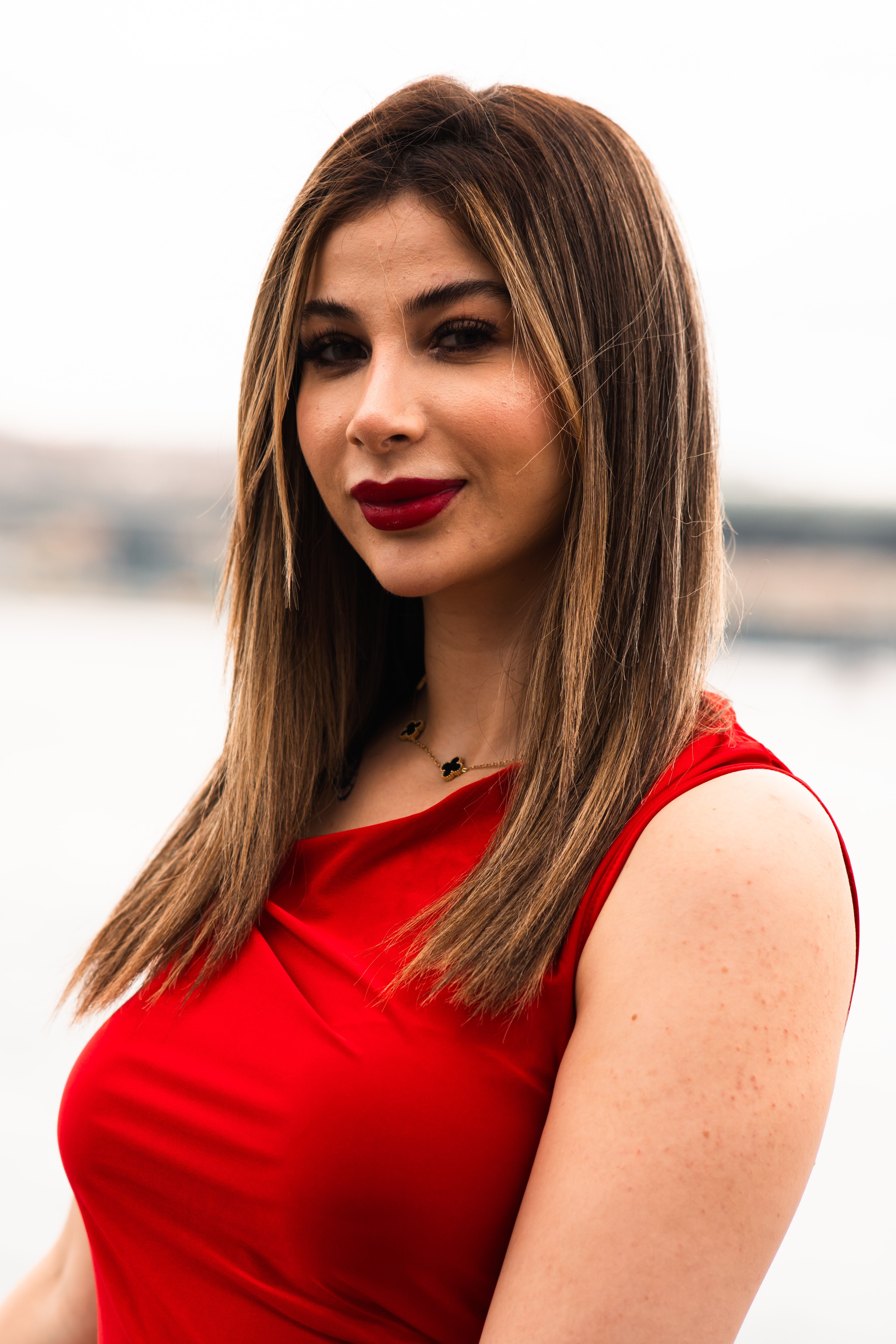 A portrait of an adult woman in a red dress posing by the Istanbul waterfront.