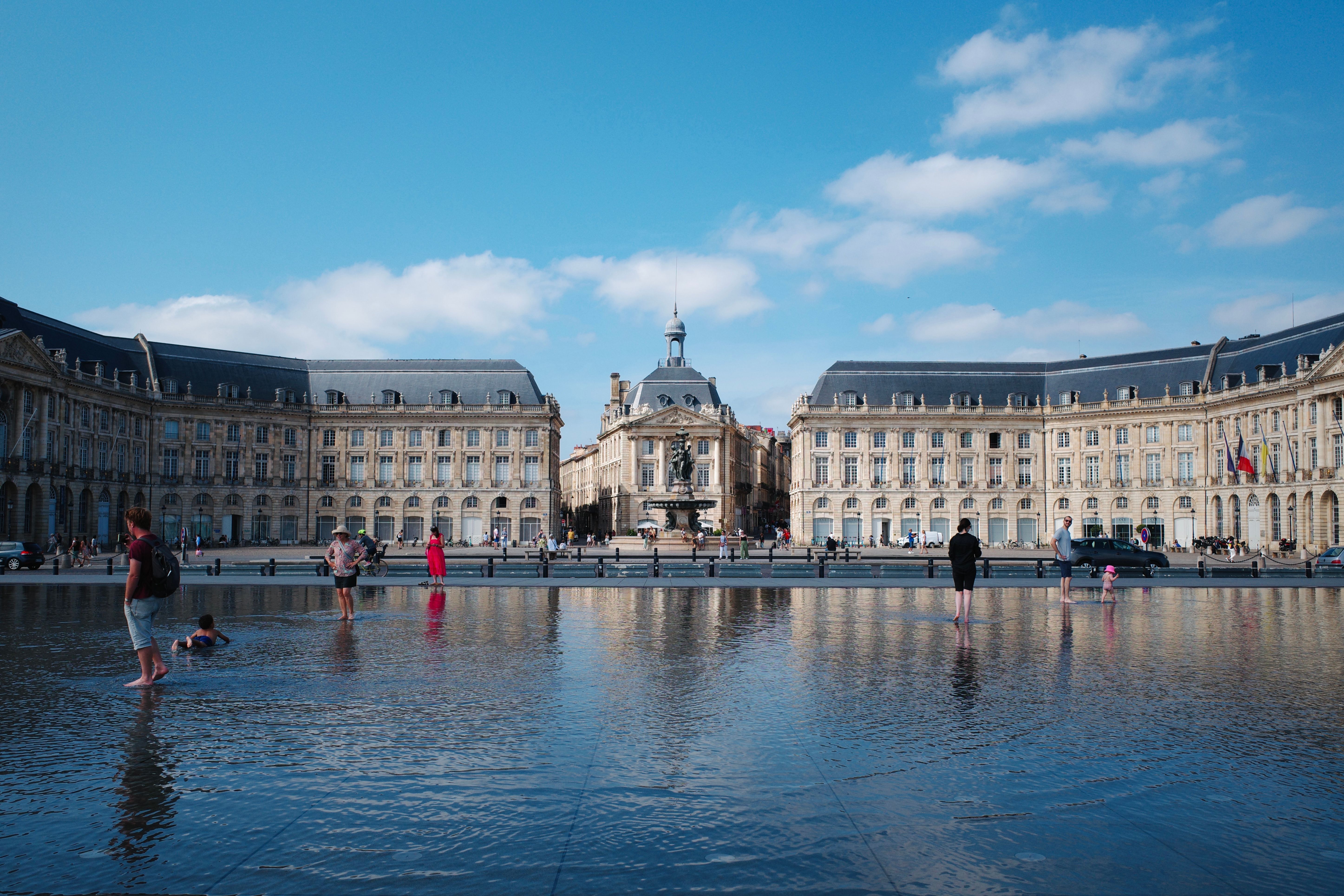 People enjoy a sunny day at Place de la Bourse in Bordeaux, France, reflected in the water mirror.