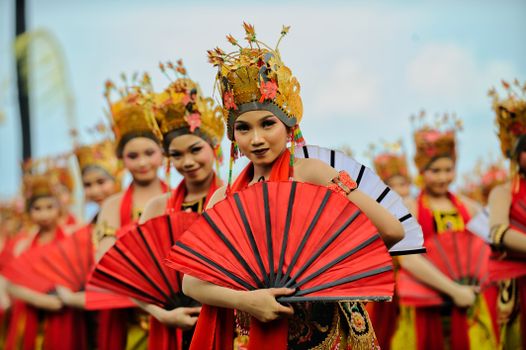 Female performers in vibrant attire and fans during a traditional Indonesian dance.