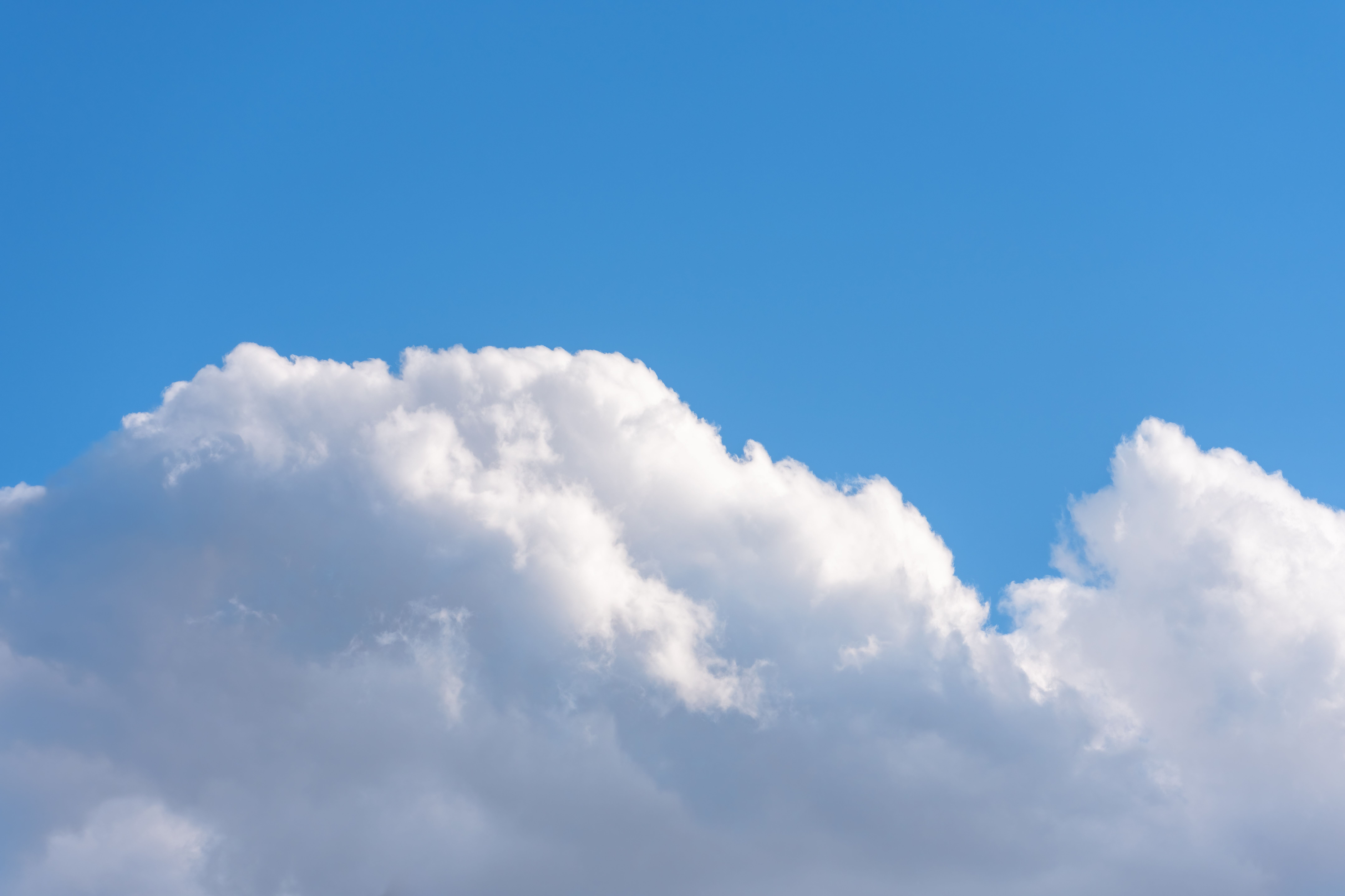 Serene sky with fluffy white clouds against a clear blue backdrop, perfect for peaceful and calm settings.