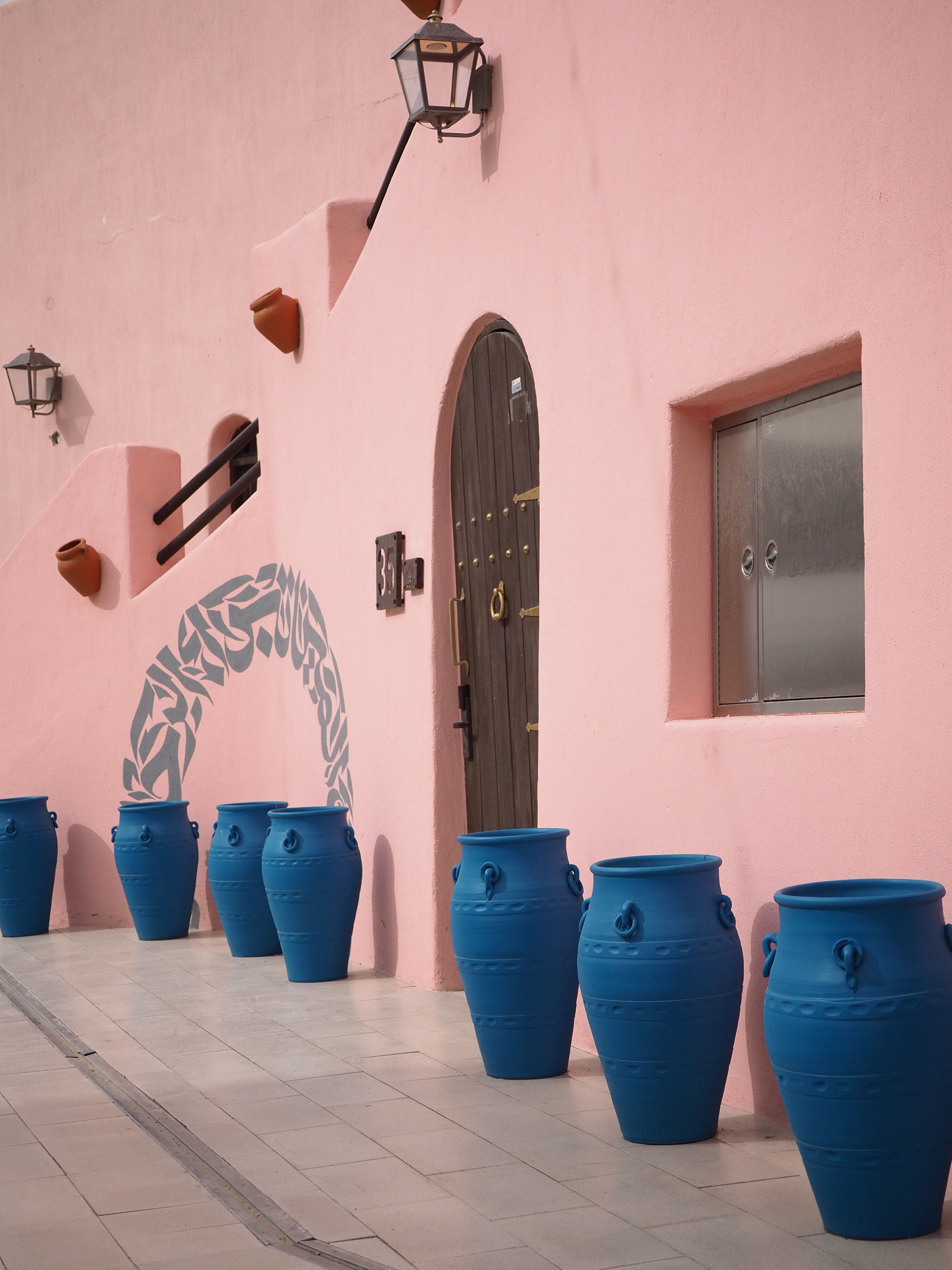 Vibrant blue pots line a traditional pink wall in Qatar, showcasing unique architectural elements.