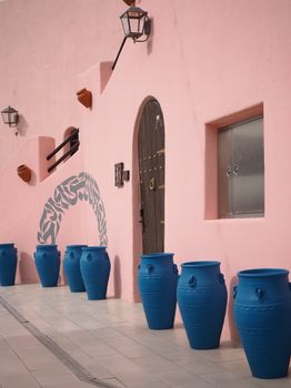 Vibrant blue pots line a traditional pink wall in Qatar, showcasing unique architectural elements.