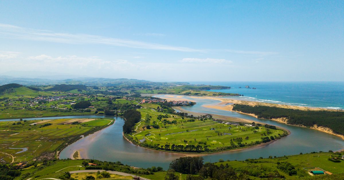 Aerial shot capturing the lush green landscape and winding river meeting the ocean along Cantabria's coastline.