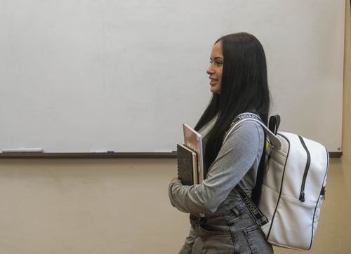 Free A young student stands by a whiteboard holding a notebook in a classroom setting. Stock Photo