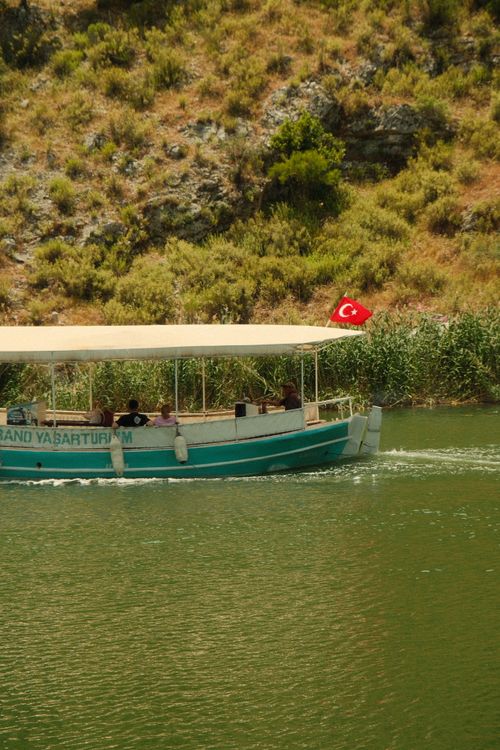 Free A boat with a Turkish flag navigates a tranquil river amidst lush greenery. Stock Photo