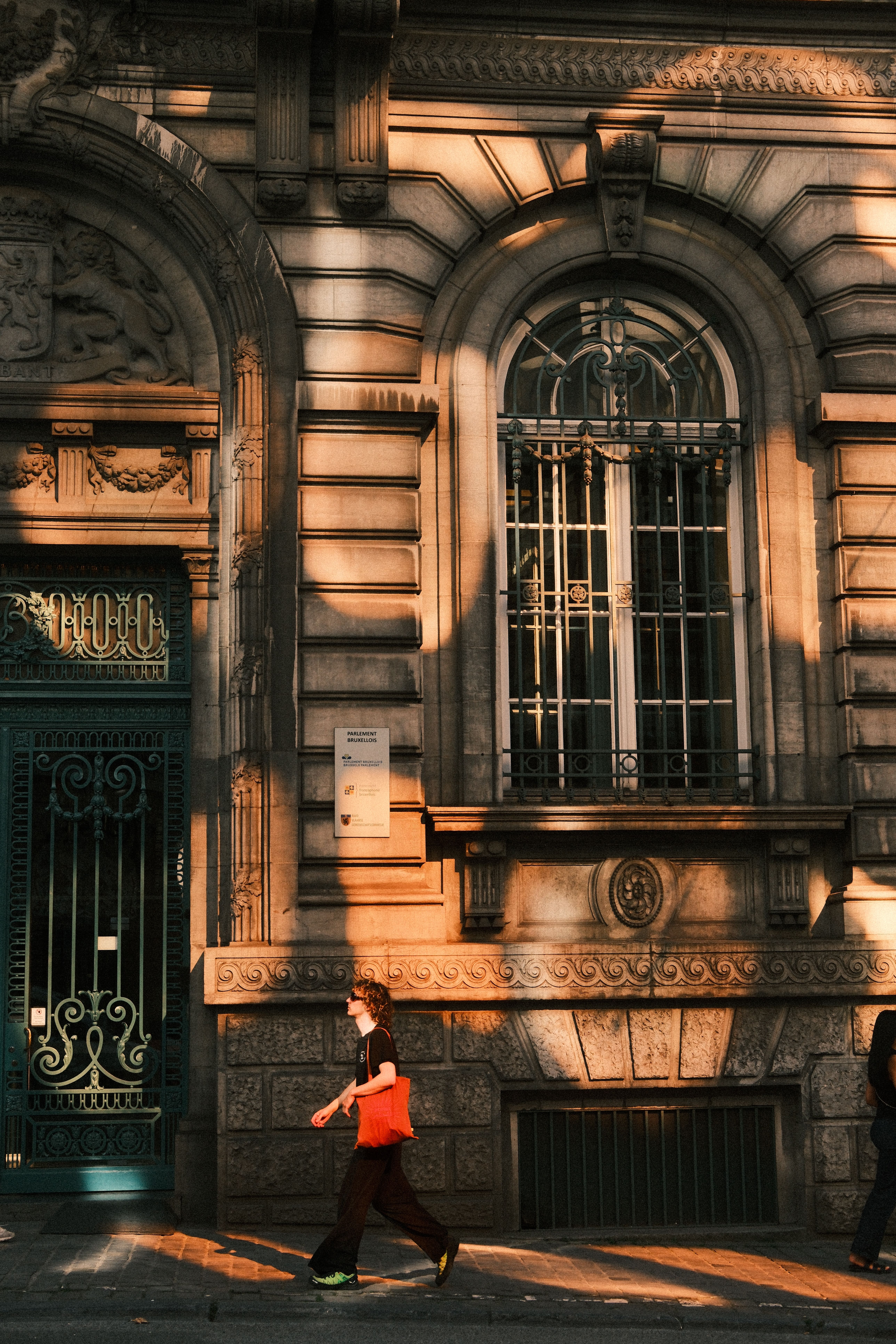 A person walks past an ornate historic building during golden hour.