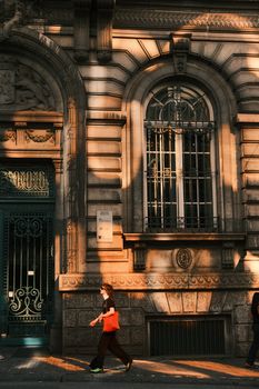 A person walks past an ornate historic building during golden hour.