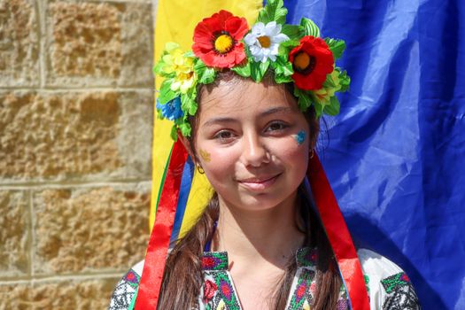 A young girl in traditional attire and a vibrant flower crown, smiling outdoors.