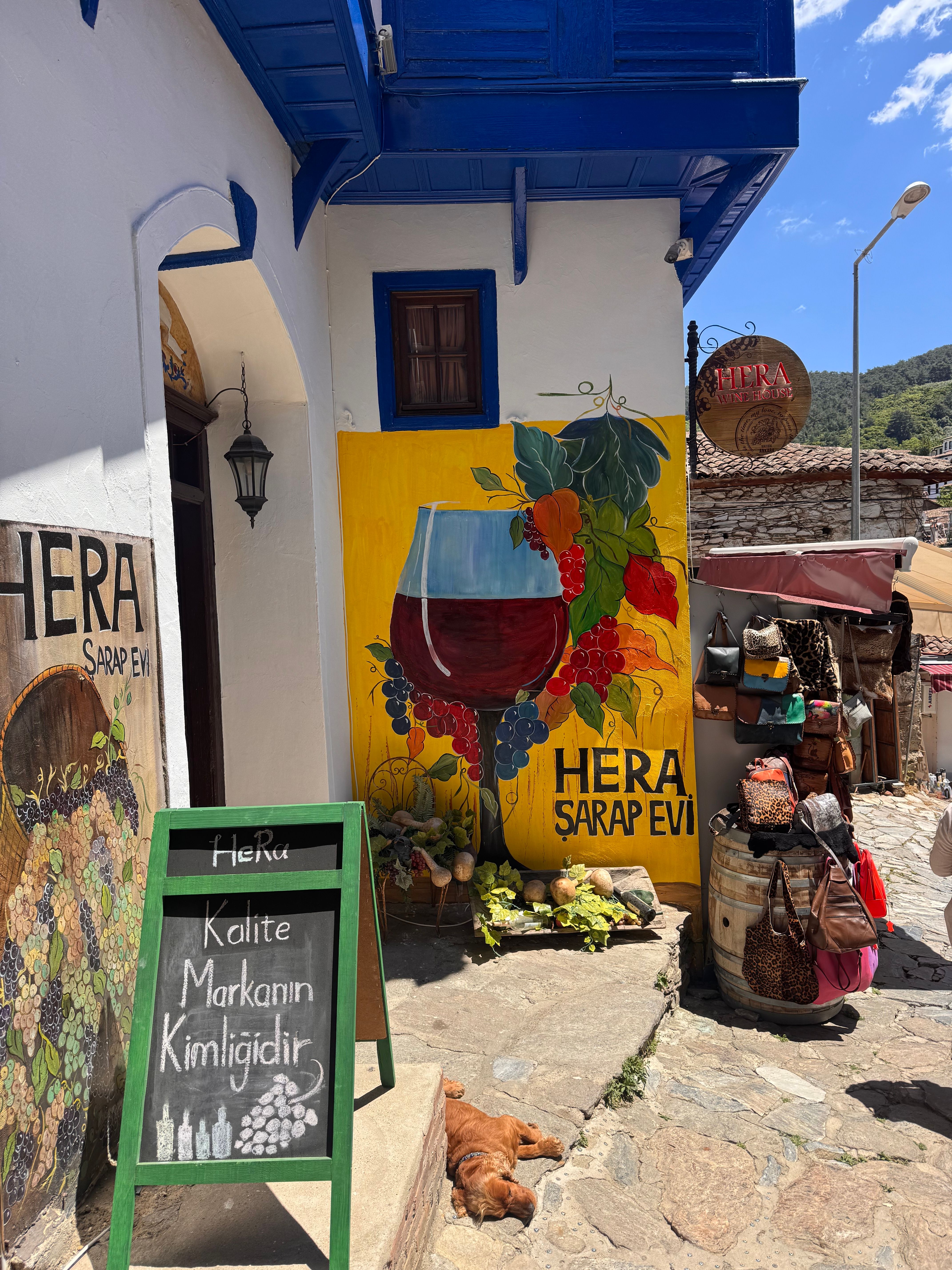 Colorful street view in Şirince, İzmir featuring the wine house Hera Şarap Evi and decorative displays.