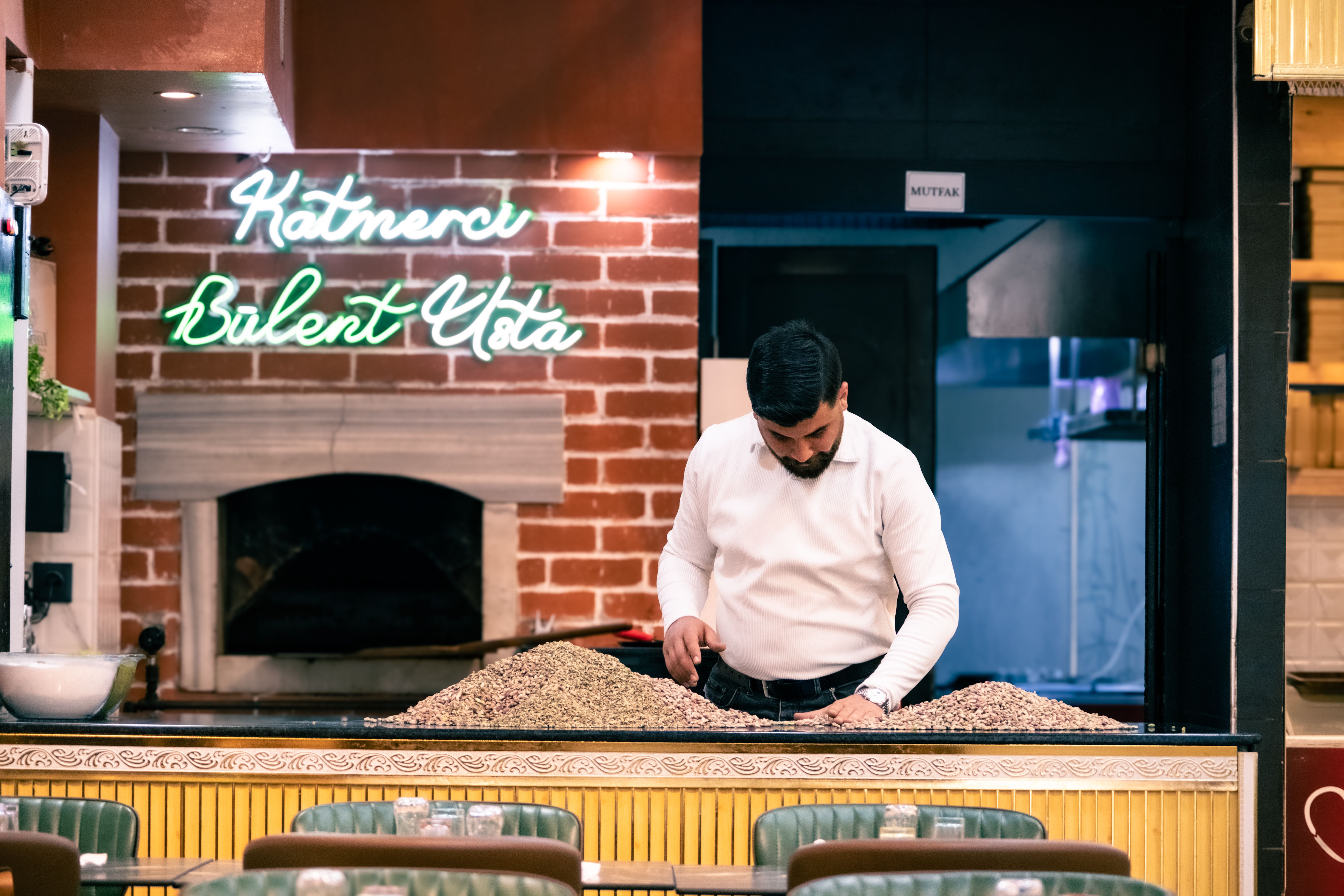 A chef preparing traditional Turkish food in a cozy restaurant setting with a neon sign in the background.