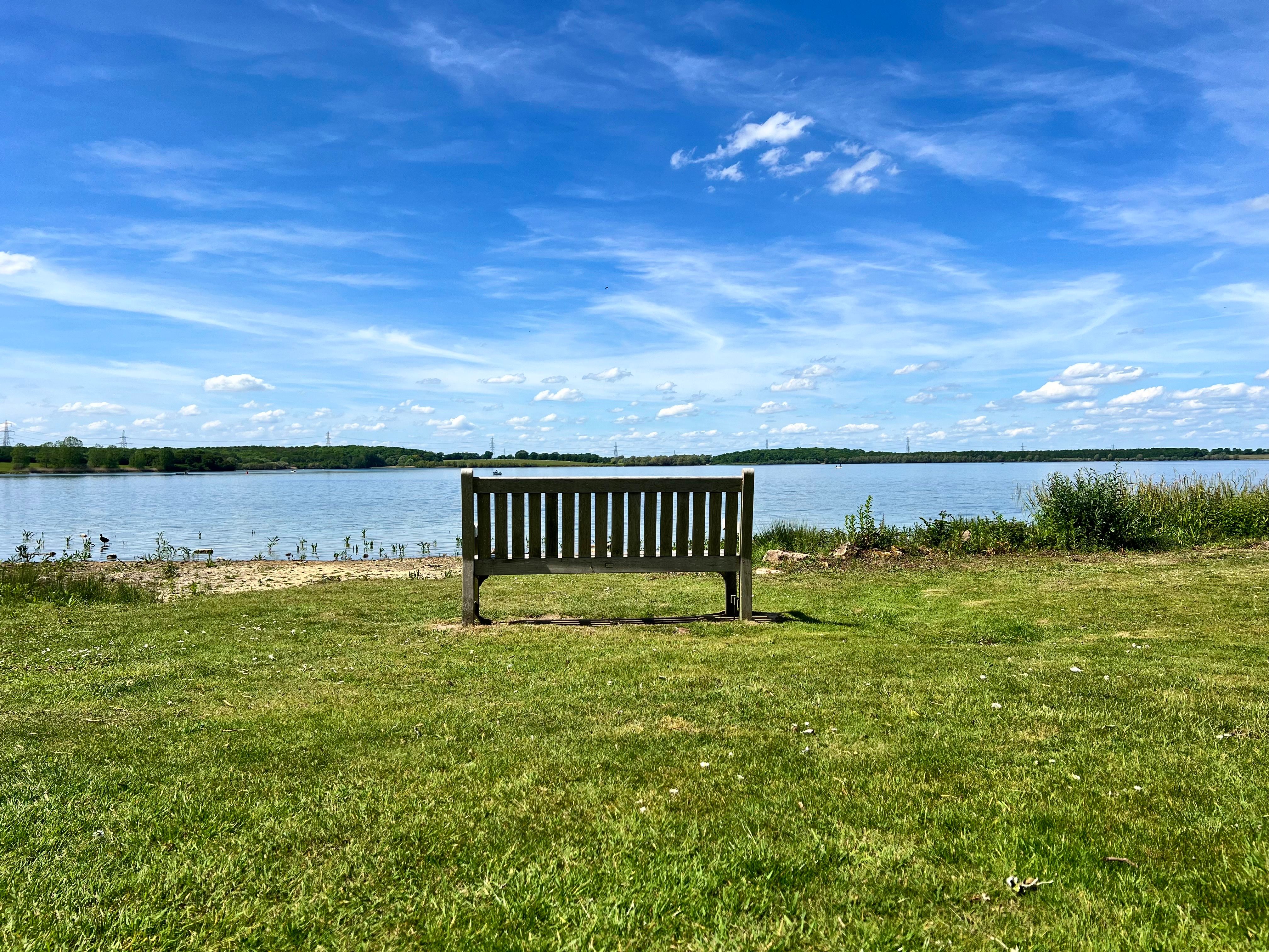 Tranquil scene of a wooden bench by a lake under a clear blue sky.