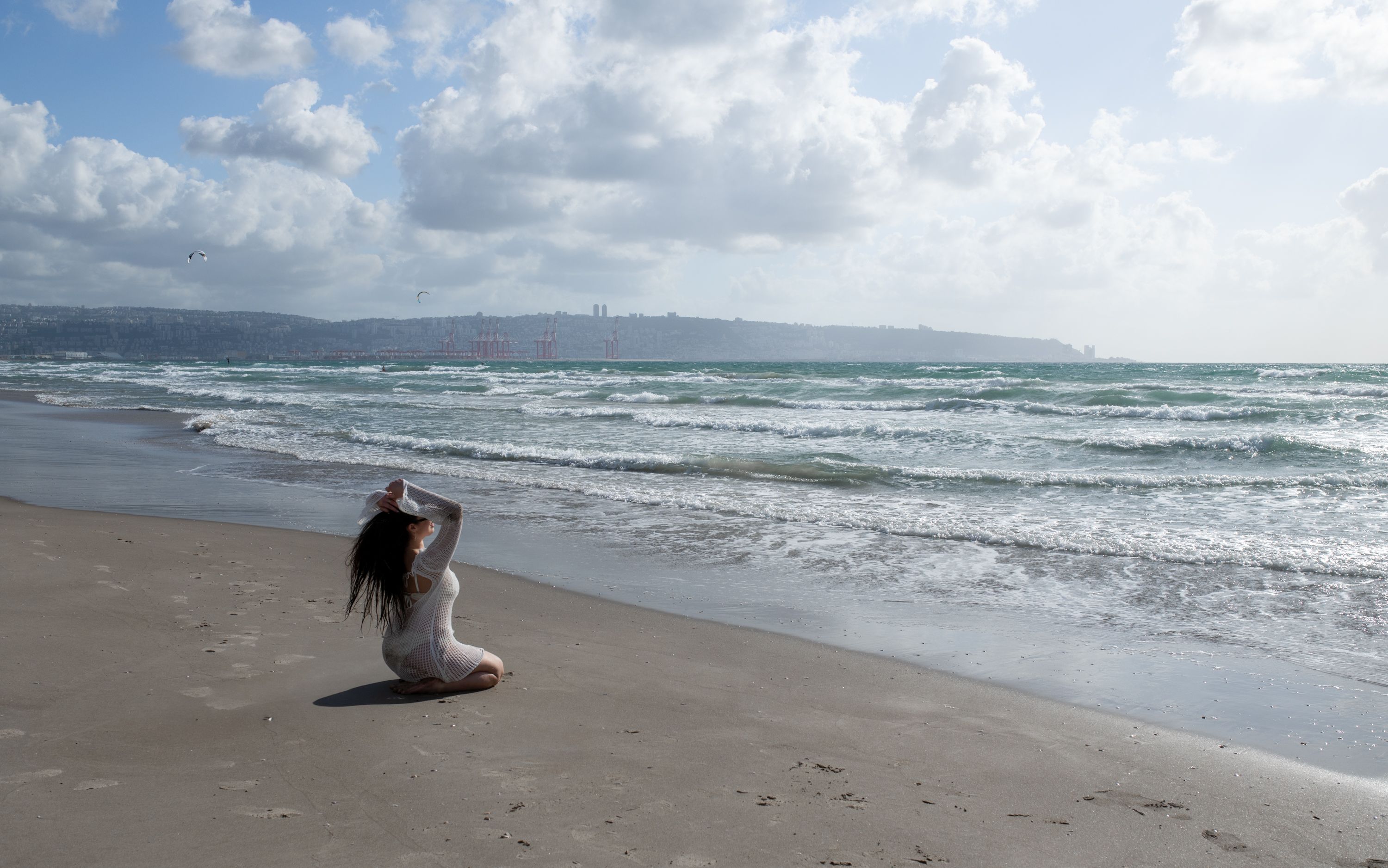 Serene beach scene with a woman meditating, waves crashing and soft clouds in the blue sky.