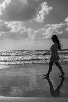 A serene black and white silhouette of a woman walking along the beach at sunrise.