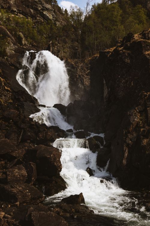 Free A stunning waterfall in Norway flows through rugged rocks surrounded by lush greenery. Stock Photo