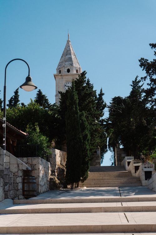 Free A picturesque stone pathway with a historic church tower in a sunny outdoor setting. Stock Photo
