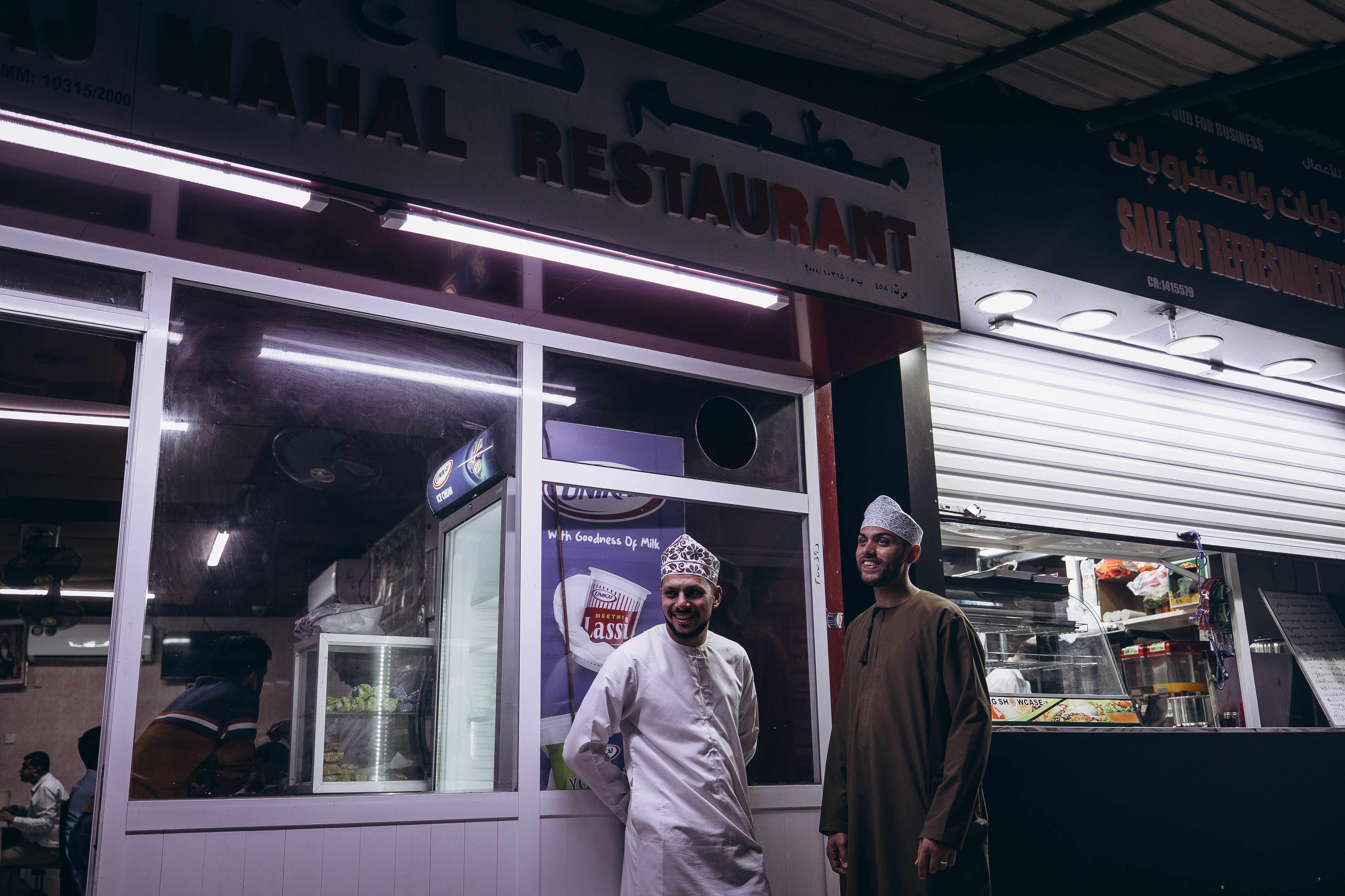 Two men in traditional attire enjoy the vibrant nightlife at a Muscat restaurant.